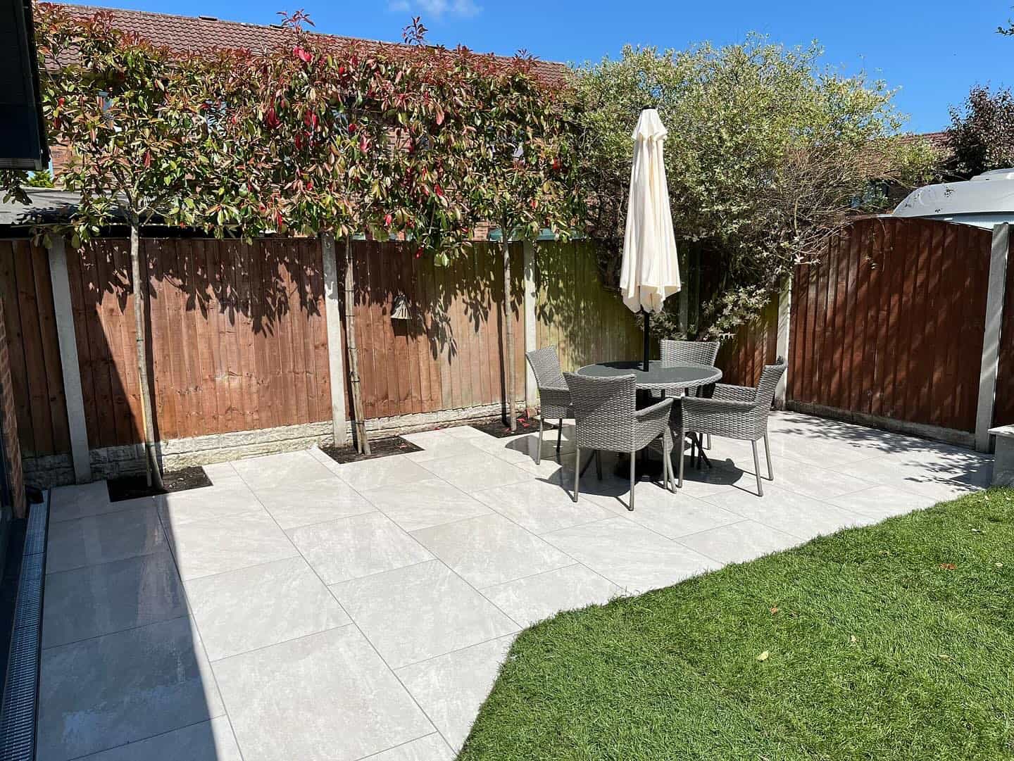 Outdoor patio featuring Rasa White Matte 24x24x2cm Rectified Porcelain Paver. Elegant light-toned pavers create a polished look, complemented by modern wicker furniture and lush greenery. Ideal for stylish, durable hardscape projects and garden patios.