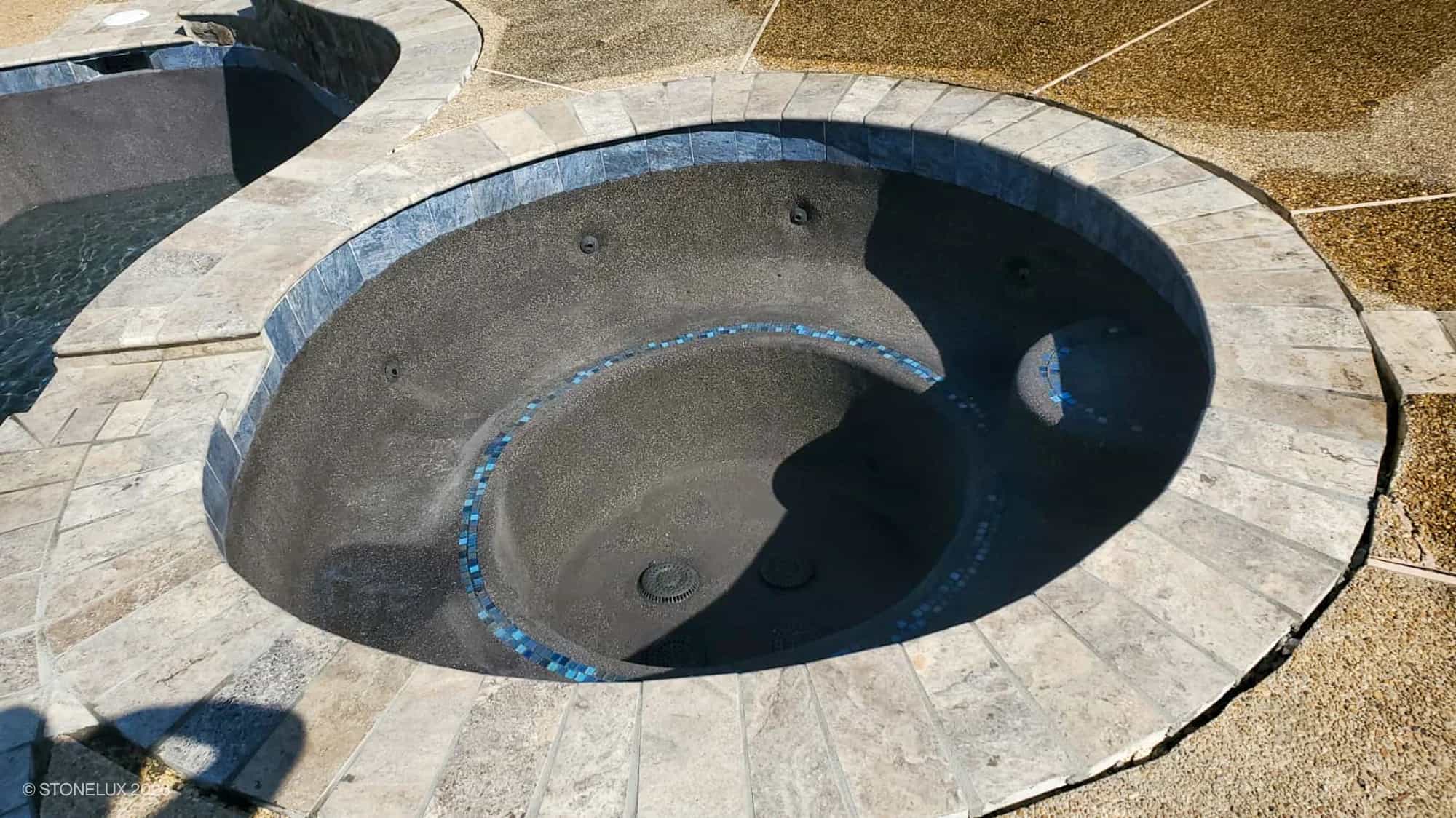 Silver Travertine Tumbled 6x12x3cm Single Bullnose Coping installed around a pool edge, showcasing its natural stone texture and light grey tones. Complements dark pool interior and textured deck, ideal for modern hardscape and pool designs.