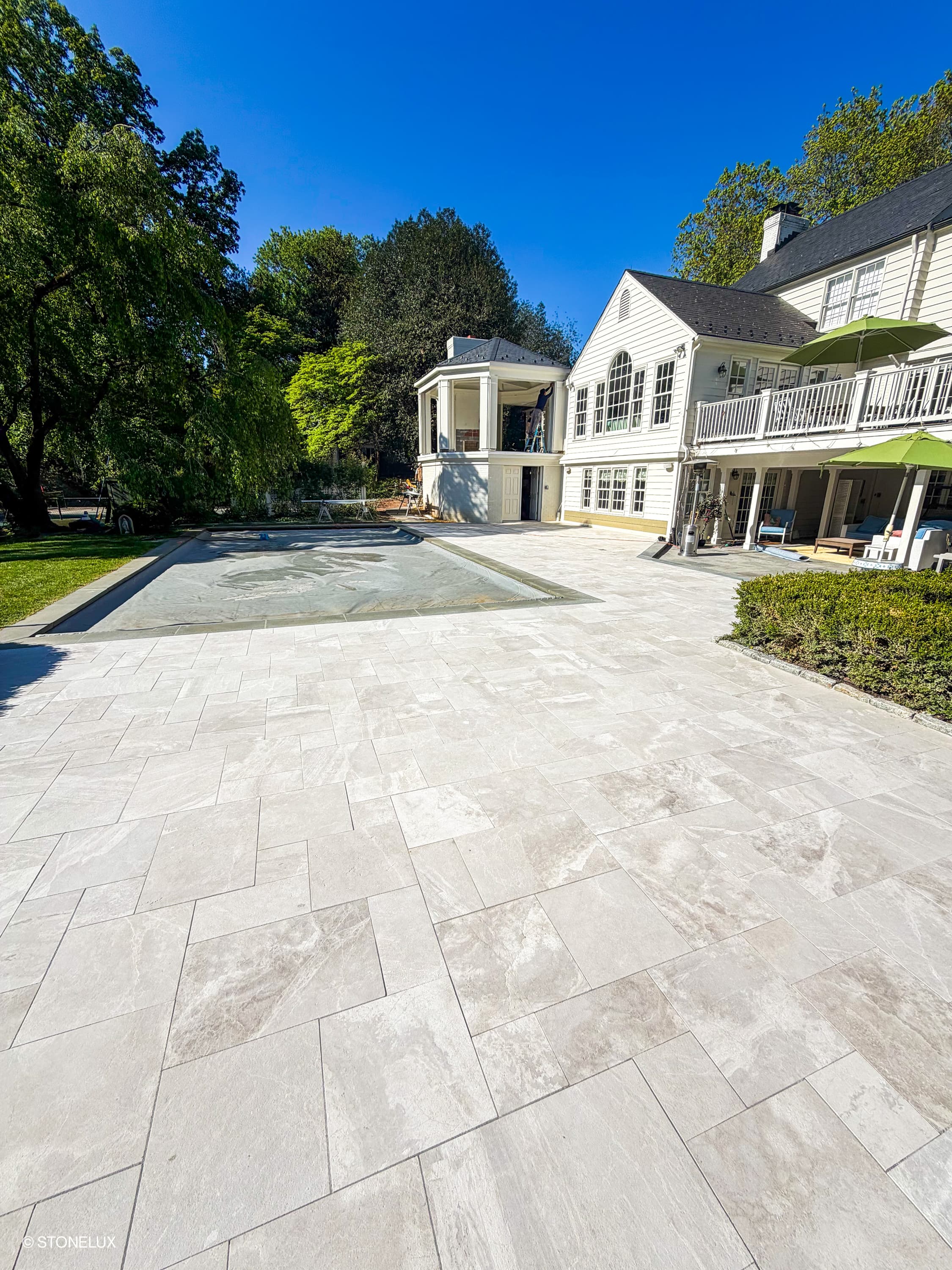 Luxurious outdoor patio featuring Pera Cream Marble Sand Blasted French Pattern 3cm Paver by STONELUX. The light, textured marble pavers complement the elegant white home and lush green landscaping, creating a sophisticated and inviting outdoor space.