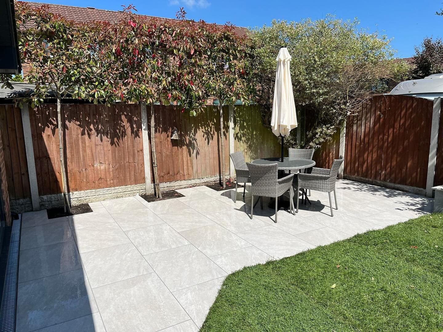 Outdoor patio featuring Rasa White Matte 24x24x2cm Rectified Porcelain Paver. Elegant light-toned pavers create a polished look, complemented by modern wicker furniture and lush greenery. Ideal for stylish, durable hardscape projects and garden patios.