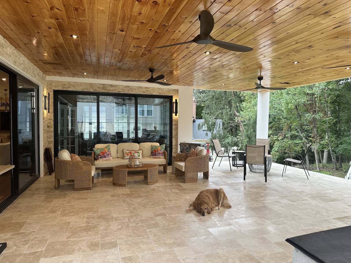Ivory Travertine Tumbled French Pattern 3cm Paver used in a luxurious patio setting. The travertine's warm, creamy tones complement the rustic wooden ceiling and wicker furniture. The spacious outdoor area is surrounded by greenery, creating a serene a...
