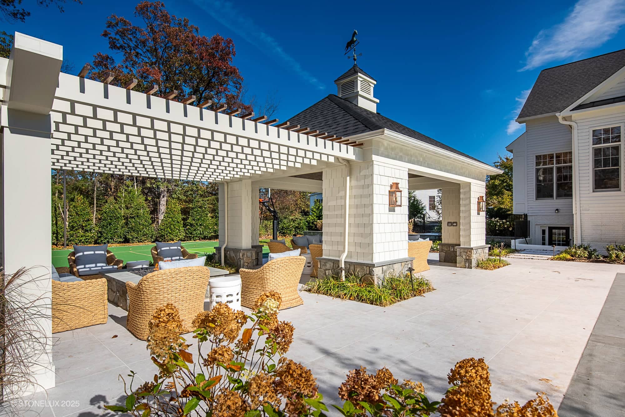 Outdoor patio featuring Pera Cream Marble pavers by STONELUX, showcasing a spacious and elegant design. The marble complements wicker furniture under a white pergola, surrounded by lush greenery, creating a luxurious and inviting hardscape.