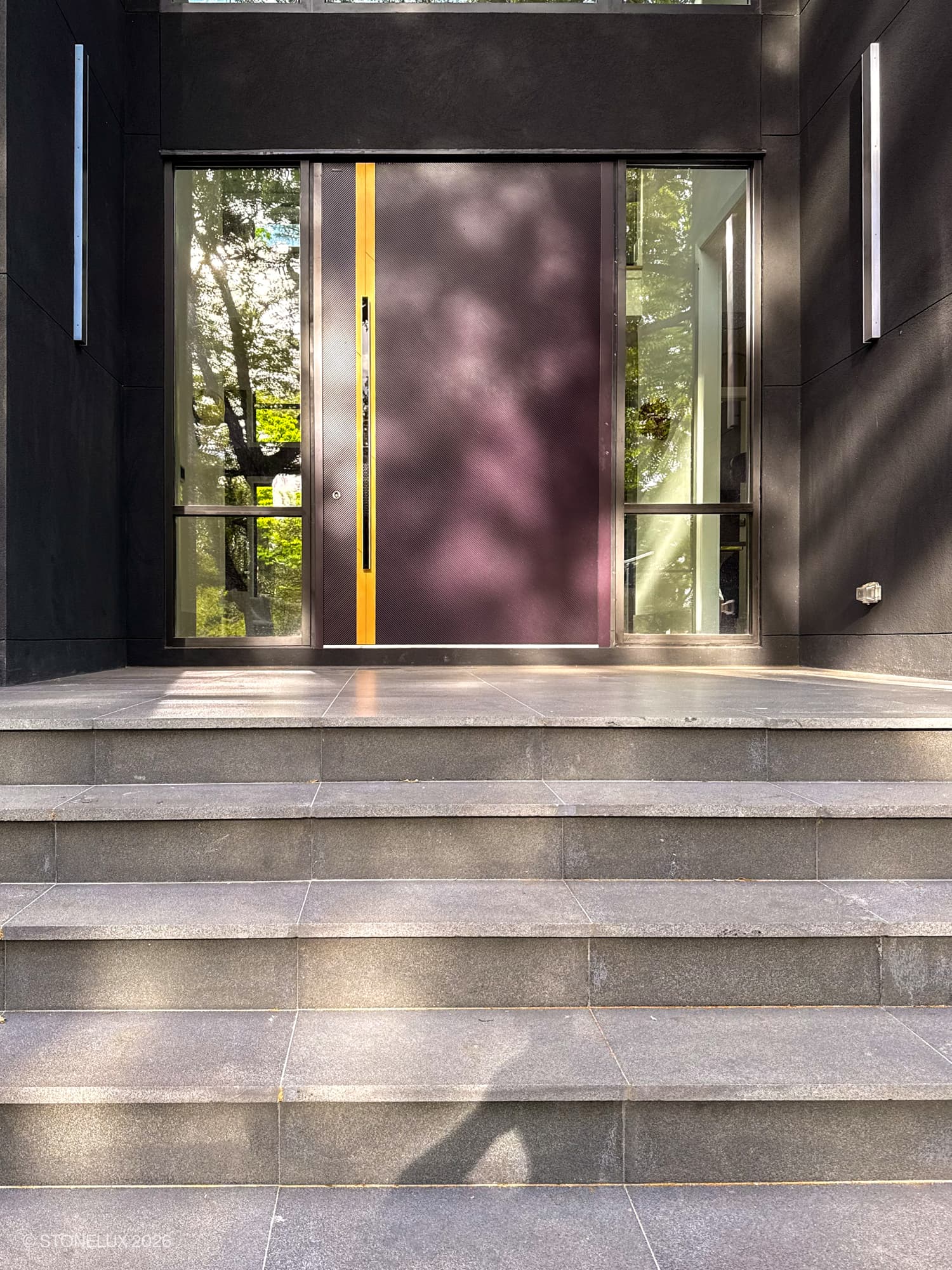 Modern entryway featuring Black Basalt Tumbled+Brushed 3cm Paver steps by STONELUX. These basalt pavers enhance the sleek design, complemented by a contemporary door and glass panels, creating a sophisticated and stylish entrance. Ideal for upscal...