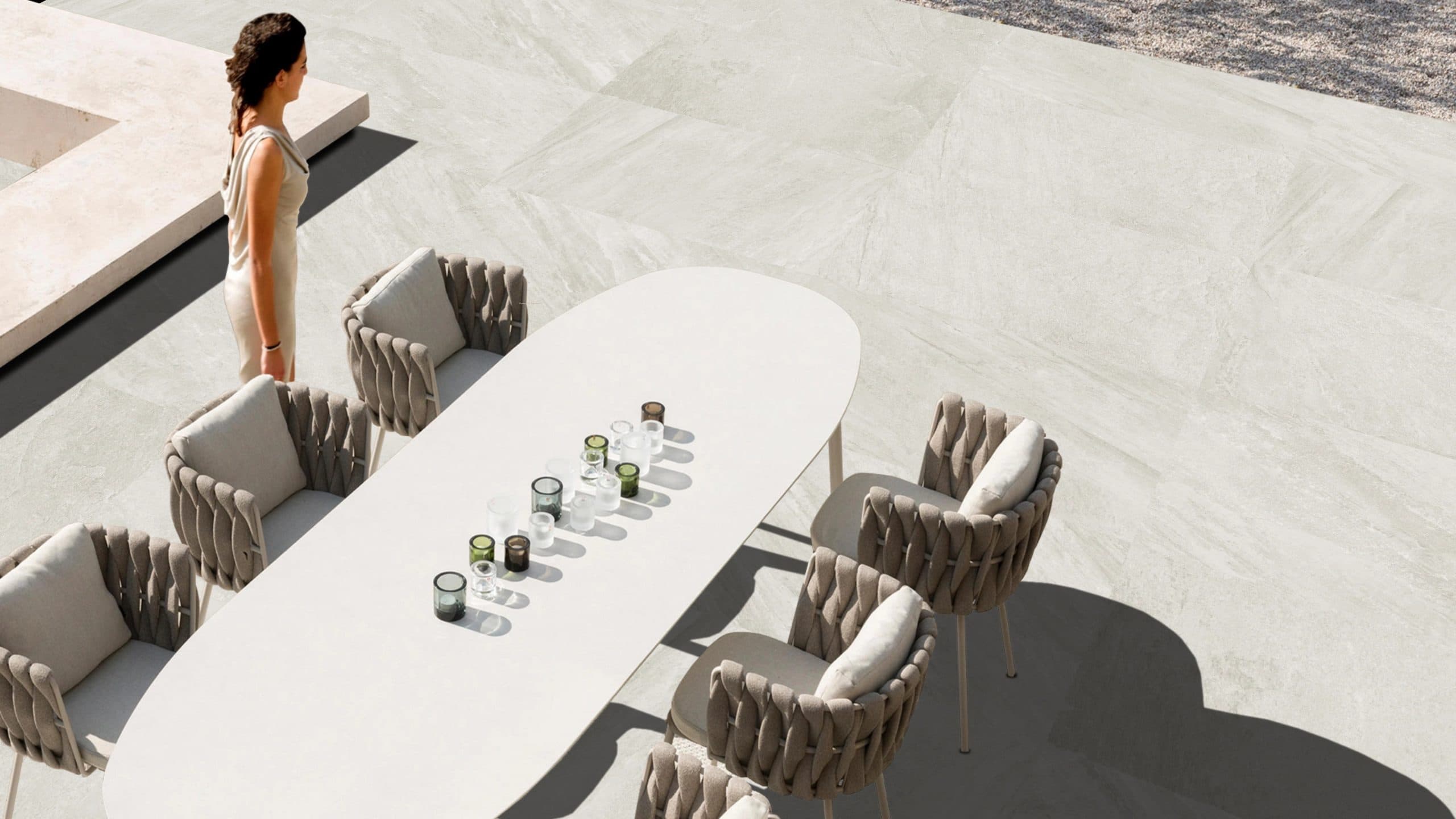 Outdoor patio scene featuring Indiana Blanco Matte 24x48x2cm Rectified Porcelain Pavers from Stonelux. The light, matte finish complements the modern setting with woven chairs and a white table, ideal for pool decks and contemporary landscapes.