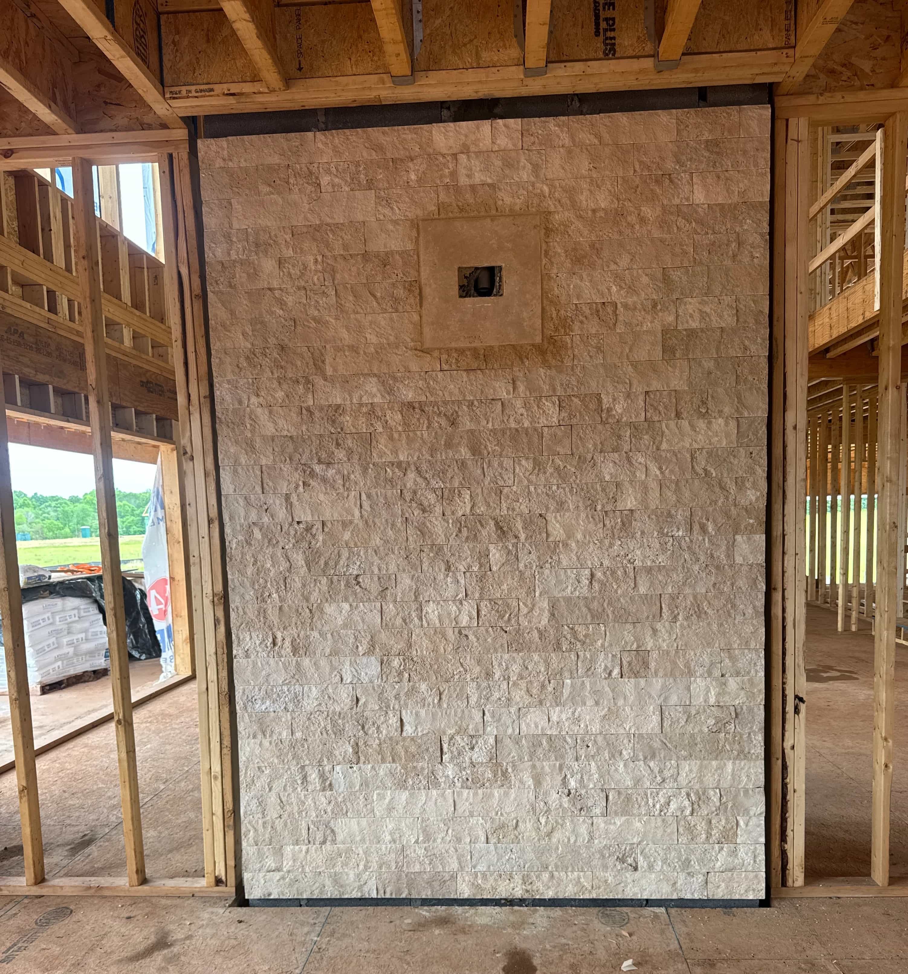 Ivory Travertine Splitface Veneer installed as an interior accent wall within a wooden-framed construction site. The natural stone features a textured, rustic surface with subtle beige tones, enhancing the unfinished architectural space. Ideal for cont...