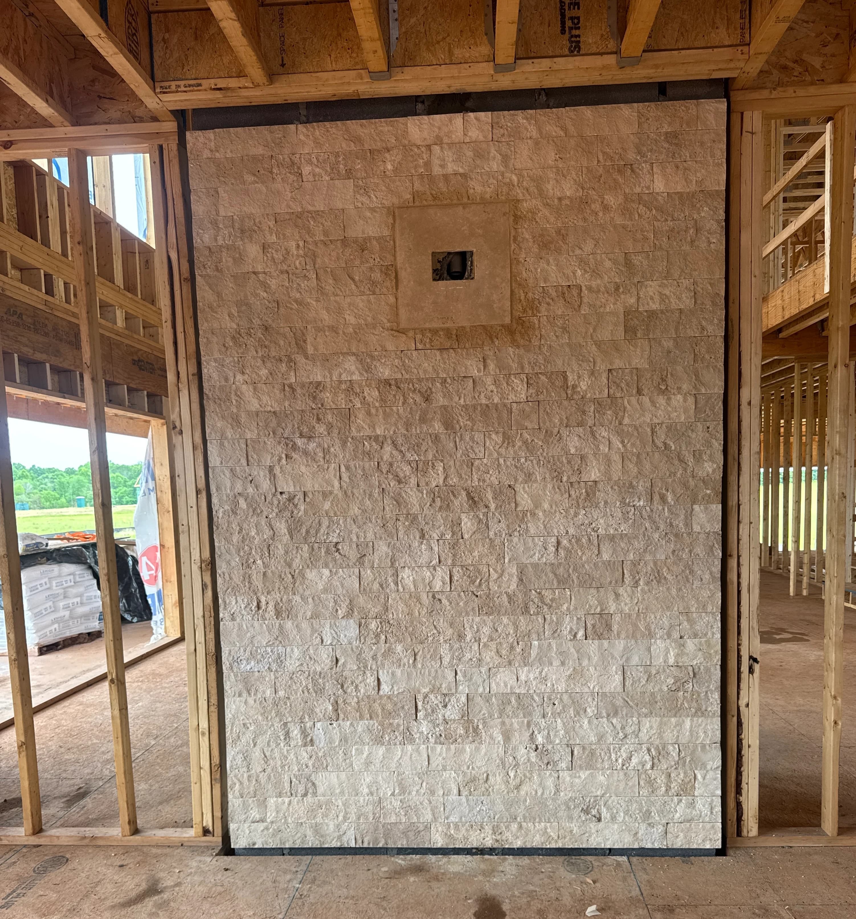 Ivory Travertine Splitface Veneer installed as an interior accent wall within a wooden-framed construction site. The natural stone features a textured, rustic surface with subtle beige tones, enhancing the unfinished architectural space. Ideal for cont...