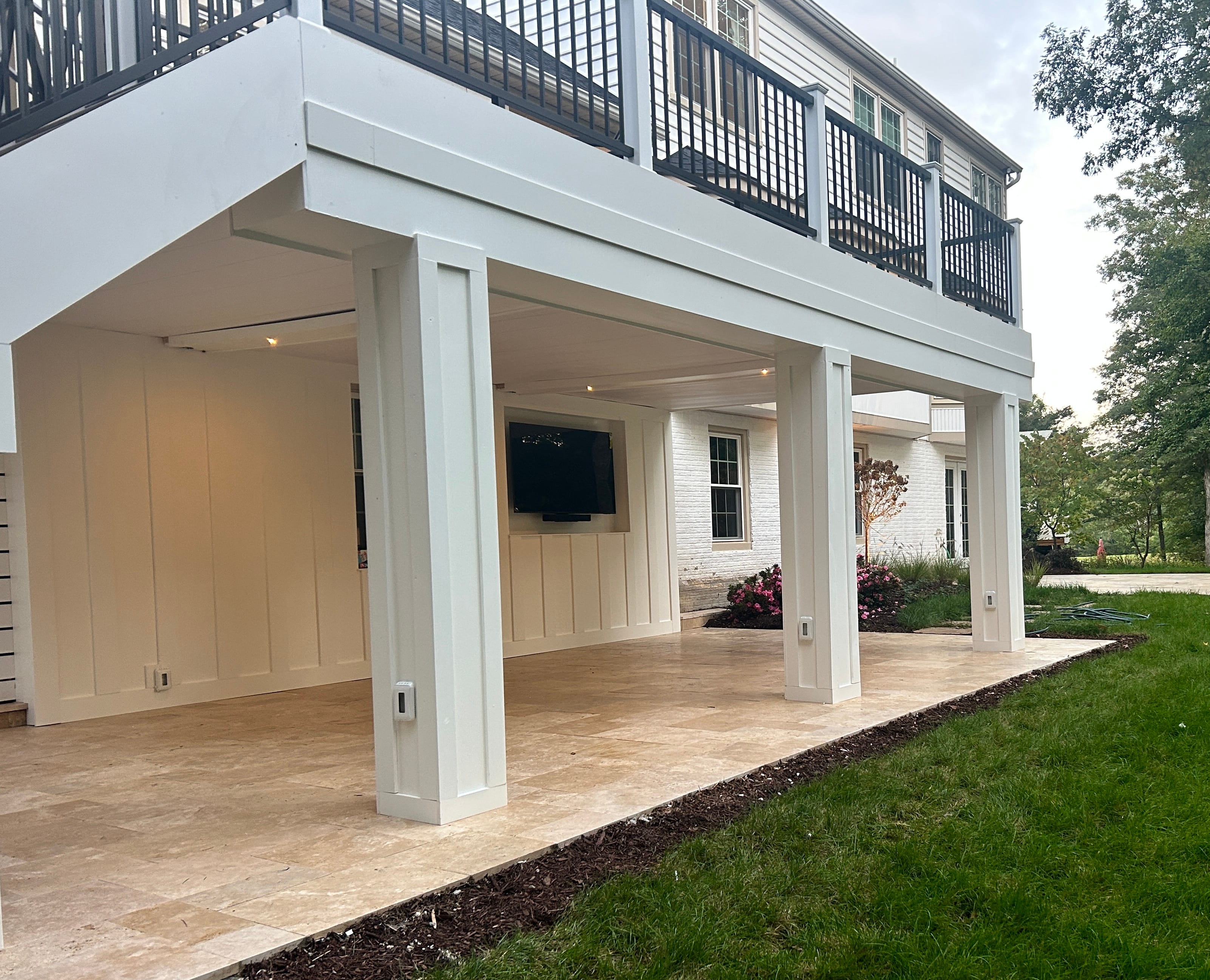 Ivory Travertine Tumbled French Pattern 3cm Paver installed on a modern patio. The natural stone's beige tones complement the white facade and black railing. Surrounded by lush greenery and classic architecture, ideal for pool decks and outdoor living ...