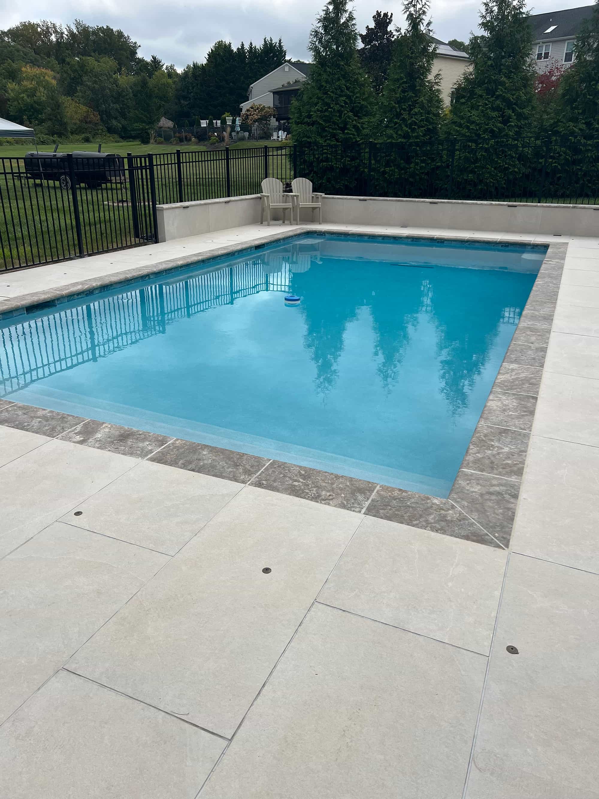 Luxurious poolside scene featuring Overland Sand Matte 24x48x2cm Rectified Porcelain Pavers. The matte porcelain finish complements the clear blue pool water, surrounded by lush greenery and black fencing, creating a modern, serene outdoor space.