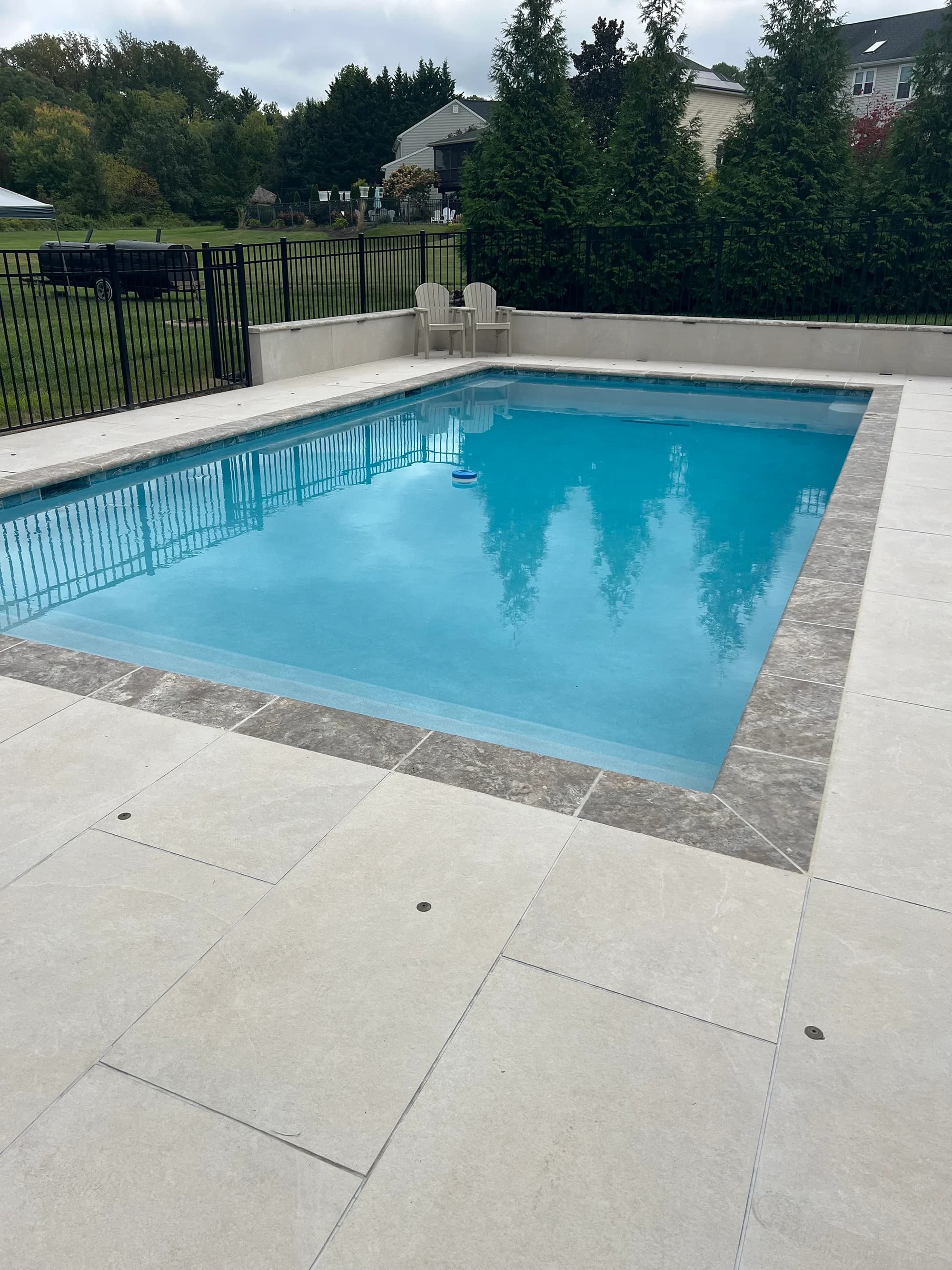 Luxurious poolside scene featuring Overland Sand Matte 24x48x2cm Rectified Porcelain Pavers. The matte porcelain finish complements the clear blue pool water, surrounded by lush greenery and black fencing, creating a modern, serene outdoor space.