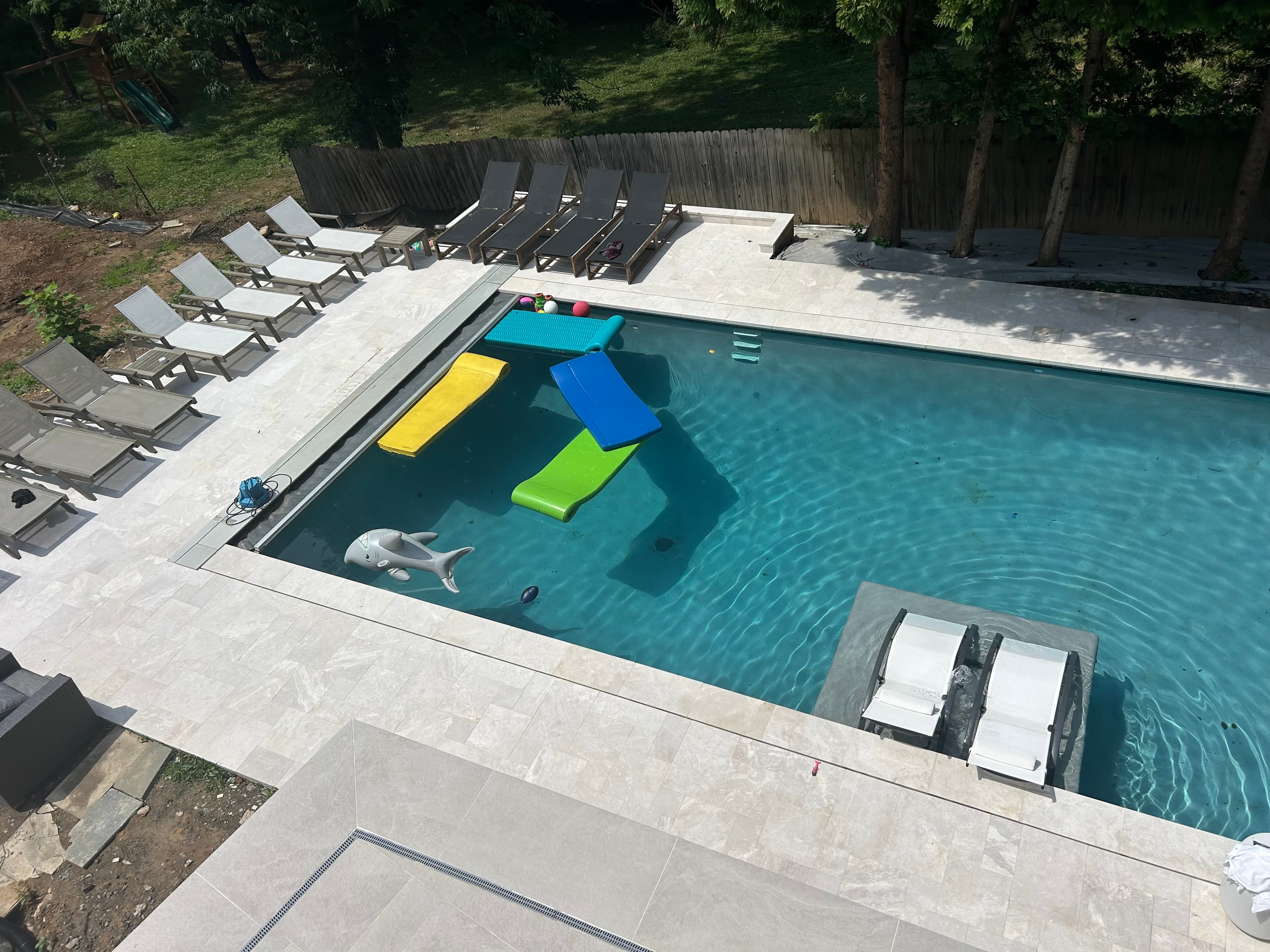 Luxurious poolside installation featuring STONELUX's Pera Cream Marble Sand Blasted French Pattern 3cm Paver. The sandblasted marble pavers complement the clear blue pool, surrounded by elegant lounge chairs and lush greenery, creating a serene outdoor...