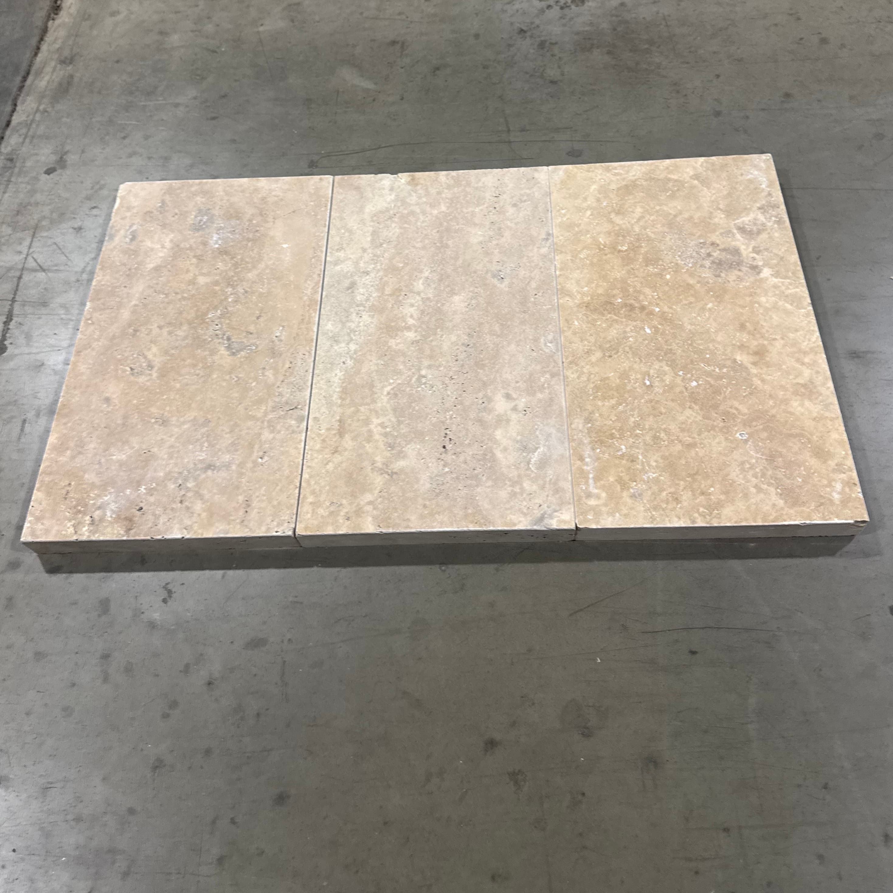 Close-up of Philly Travertine Tumbled 16x24x2 Eased Edge Coping. The natural stone features a soft, beige color with subtle veining and a textured, tumbled finish, ideal for pool coping and patio edges in luxury hardscape projects.