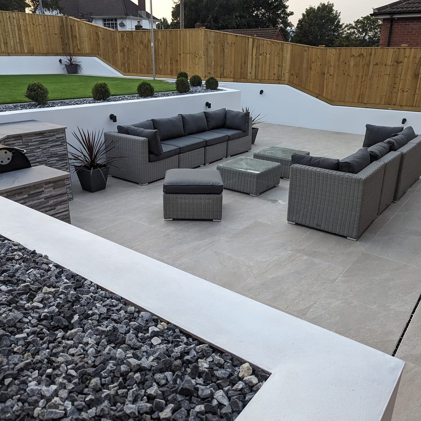 Outdoor patio featuring Rasa Beige Matte 24x24x2cm Rectified Porcelain Pavers by STONELUX. The elegant beige pavers enhance the modern setup with grey wicker sofas, glass-topped tables, and minimalist landscaping, creating a sophisticated outdoor livin...