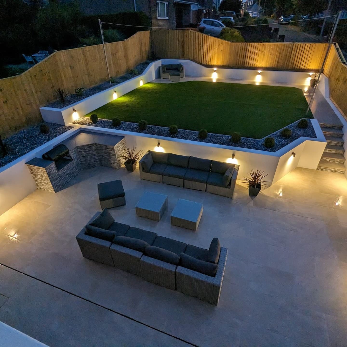 Modern outdoor patio featuring Rasa Beige Matte 24x24x2cm Rectified Porcelain Pavers. The elegant setting includes cozy seating, soft lighting, and a lush green lawn, creating a stylish and inviting ambiance perfect for entertaining or relaxing.