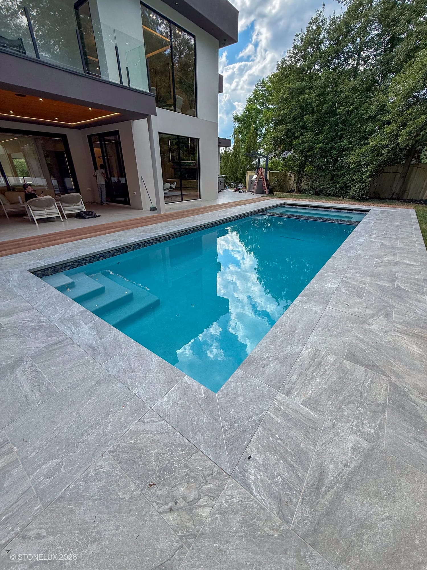 Modern pool deck featuring STONELUX Rasa Gray Matte 24x48x2cm Rectified Porcelain Pavers. The pavers' subtle gray tones and matte finish complement the clear blue pool water and contemporary home architecture, creating a seamless outdoor oasis.