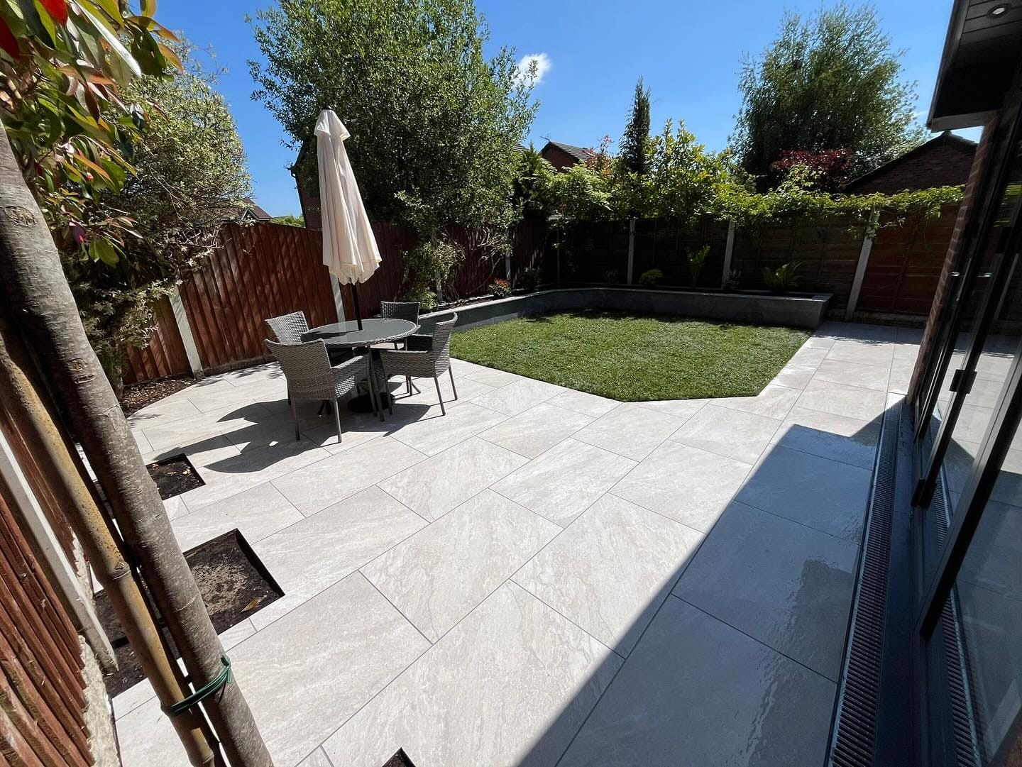 Outdoor patio featuring Rasa White Matte 24x36x2cm Rectified Porcelain Pavers by STONELUX. The sleek, light-toned pavers enhance the modern design, complementing the lush greenery and wicker furniture, ideal for luxurious hardscape projects and renovat...