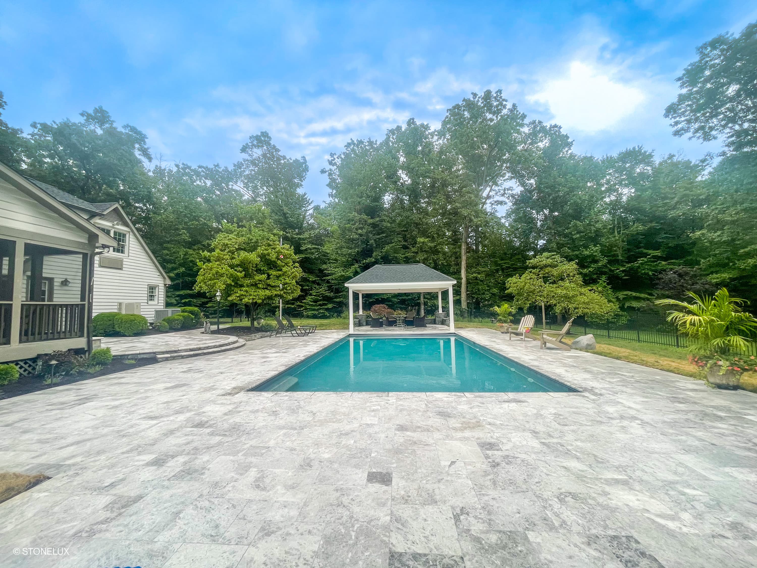 Luxurious outdoor pool area featuring Tundra Grey Marble Sand Blasted French Pattern 3cm Pavers. The elegant marble pavers complement the serene blue pool, surrounded by lush greenery and classic architecture, perfect for premium hardscape projects.
