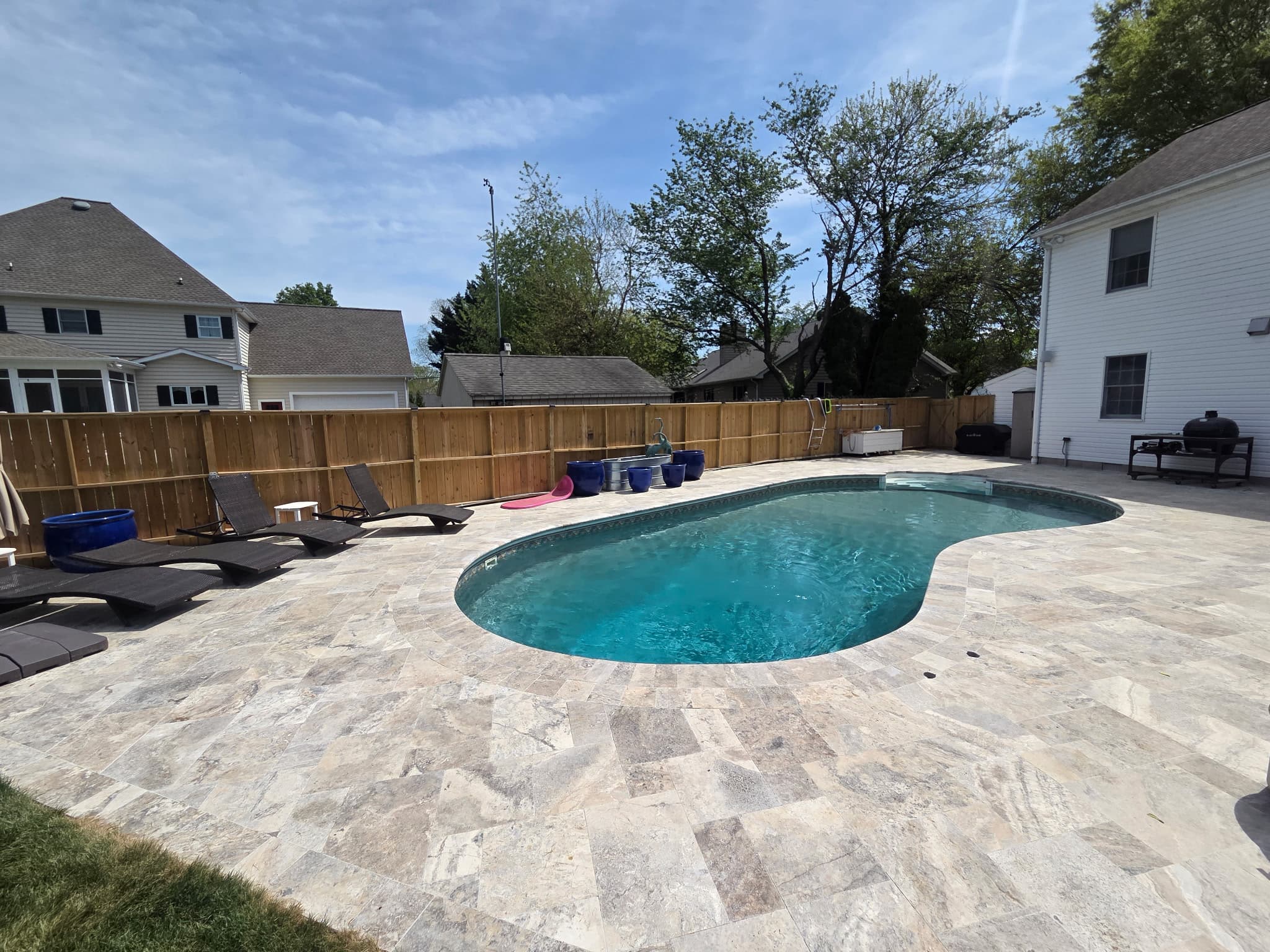 Outdoor pool area featuring Silver Travertine Tumbled French Pattern 3cm Paver - Select by STONELUX. The natural stone pavers create a stylish pool deck, complementing the clear blue water. Surrounded by modern lounge chairs and a wooden fence, enhanci...