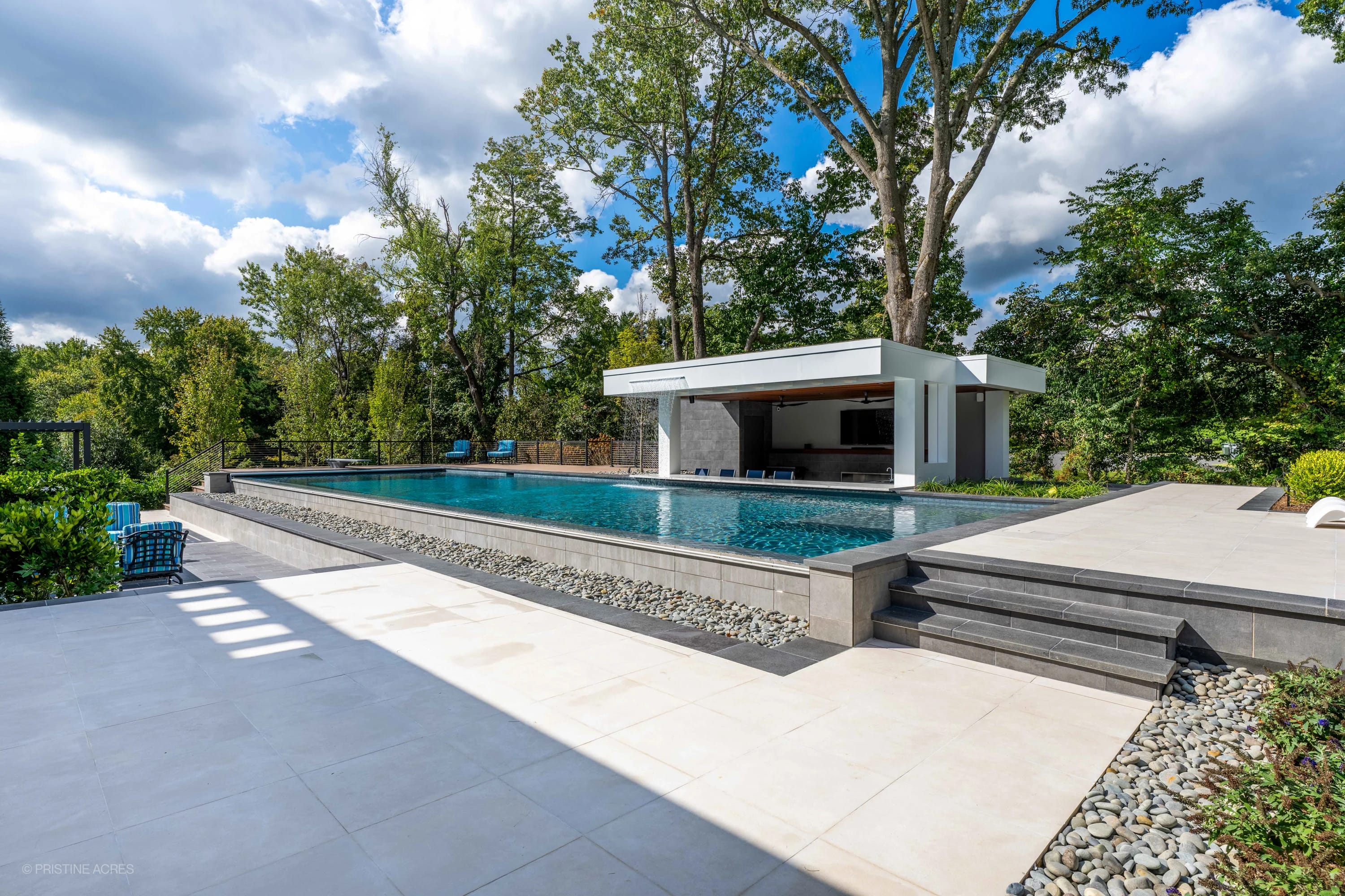 Modern McLean Pool Project featuring Black Basalt steps and Nexus White Porcelain pavers. The sleek design integrates a shimmering blue pool, surrounded by lush greenery, contemporary architecture, and elegant outdoor seating in McLean, VA.