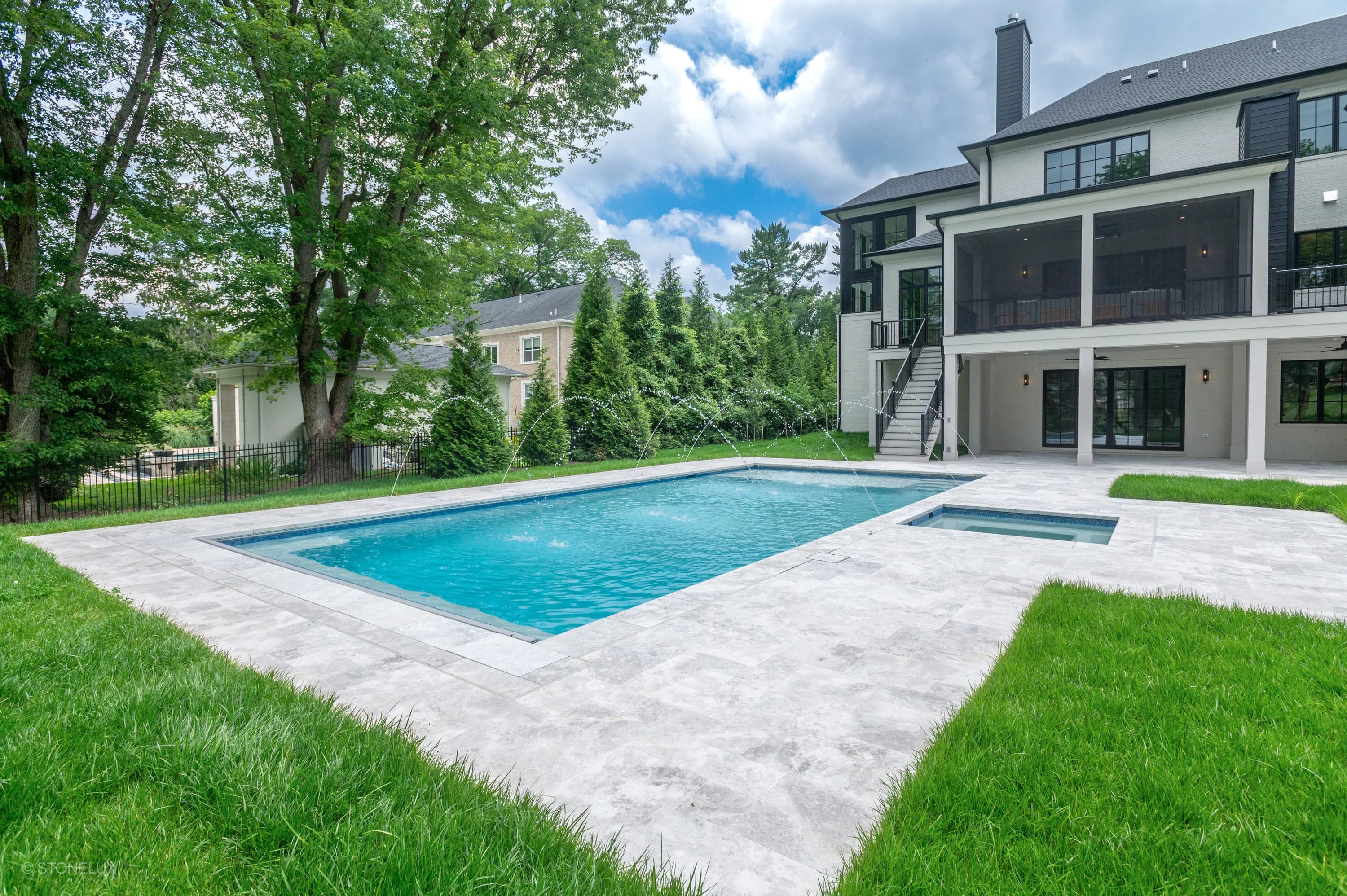 Luxurious pool retreat in McLean featuring Tundra Grey Harmony marble. The modern design boasts sleek pavers, blue pool water, and lush greenery. The elegant architecture and spacious patio create a serene backyard oasis, perfect for relaxation and ent...