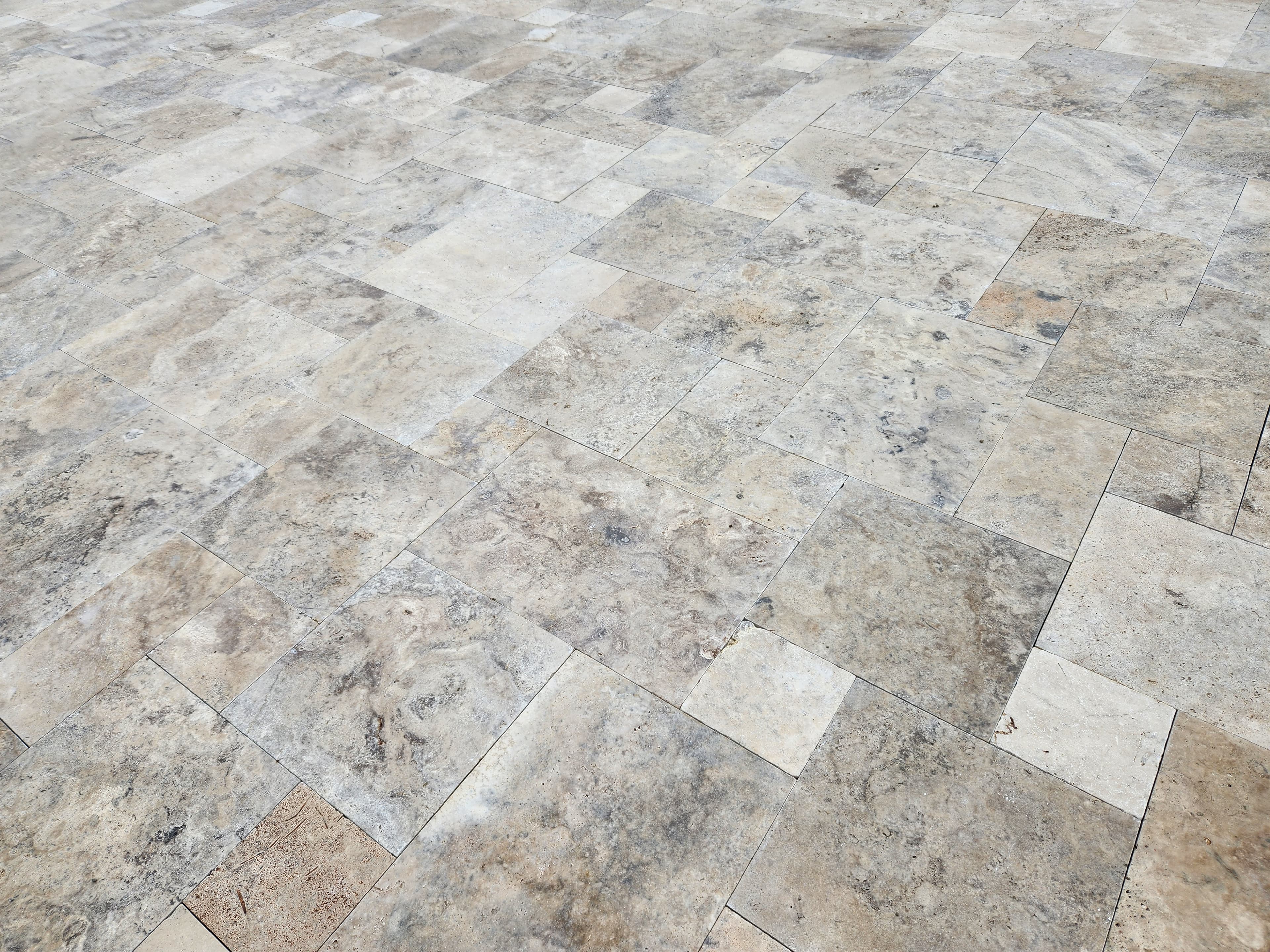A close-up view of a floor made of rectangular and square stone tiles in various shades of beige and gray, arranged in a staggered, interlocking pattern—showcasing the VA Pool & Patio Project – Philly Travertine Elegance in Winchester.