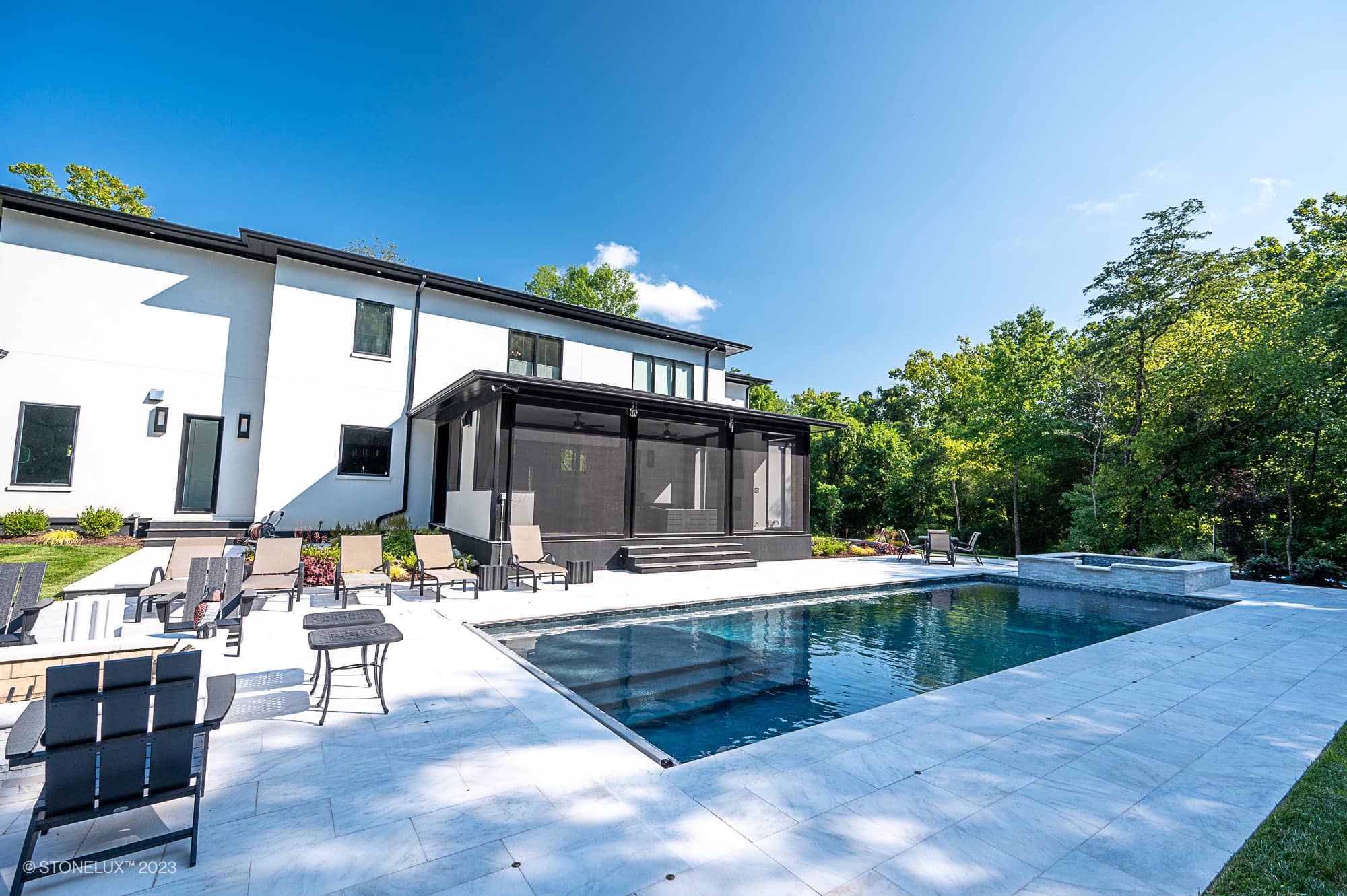 Afyon Elegance: Modern White Marvel with Black Accents poolside, this stunning house boasts a white exterior, large windows, a screened-in porch, marble patio, and in-ground pool—surrounded by trees and blue sky with stylish outdoor seating.