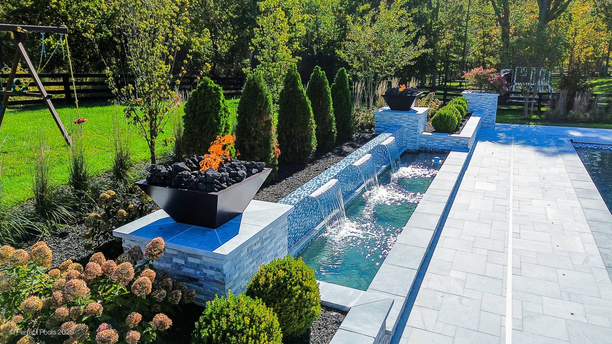 Luxury pool project in Aldie, VA featuring Aldie Serenity with Afyon White and Arctic Grey Marble. Modern design with sleek water features, lush greenery, and elegant landscaping. Grey marble pavers harmonize with tranquil blue pool water.