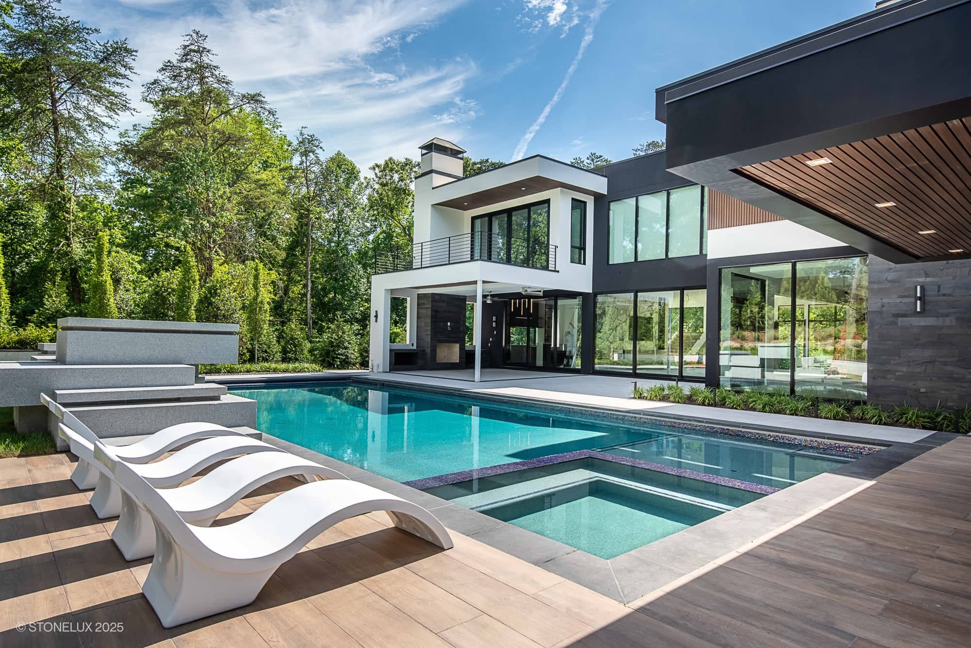 Modern Hillside Elegance – McLean Retreat with large windows, a spacious patio, and a sleek pool area finished in Overland Pearl Porcelain & Black Basalt, surrounded by greenery under a clear blue sky.