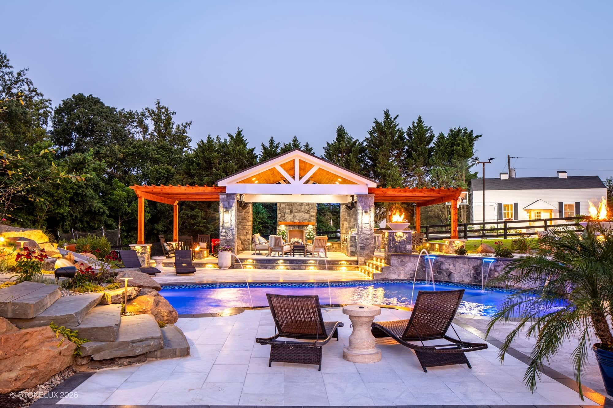Luxurious backyard oasis in McLean, VA featuring Tundra Grey Marble and Black Basalt. Modern pool with blue water, Afyon White Marble accents, surrounded by lush greenery, elegant pergola, and ambient lighting, creating a serene, upscale atmosphere.