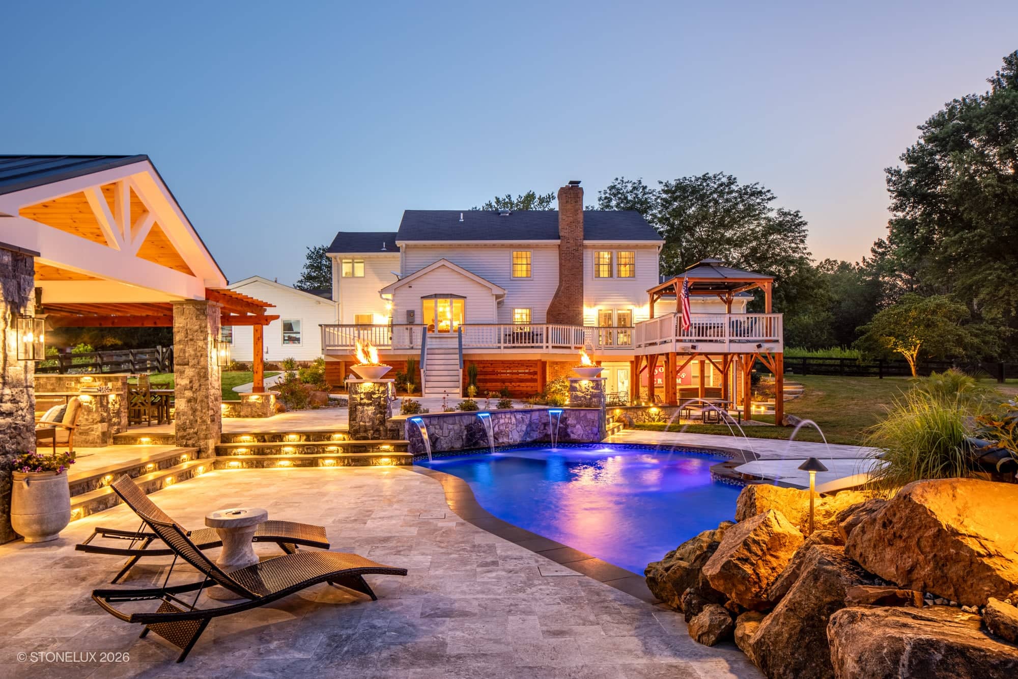 Backyard oasis in McLean, VA featuring Tundra Grey Marble and Black Basalt from Stonelux. Modern design with Afyon White Marble. Blue pool water, fire features, lounge chairs, and landscaped greenery create a serene atmosphere. Perfect for hardscape pr...