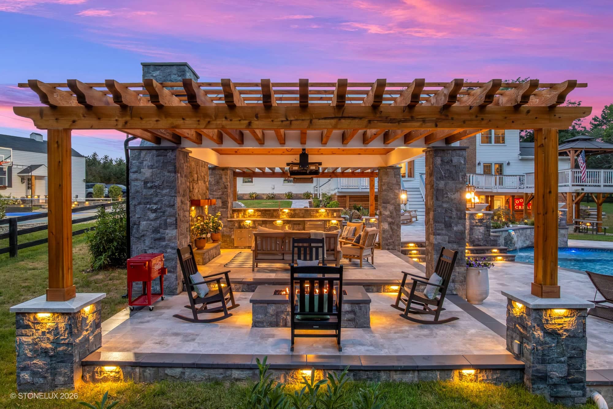 Backyard oasis in McLean, VA featuring Tundra Grey Marble and Black Basalt. A modern patio with a pergola, cozy seating, and a fire pit. The pool is complemented by lush landscaping, warm lighting, and a serene atmosphere, using Afyon White Marble. Per...