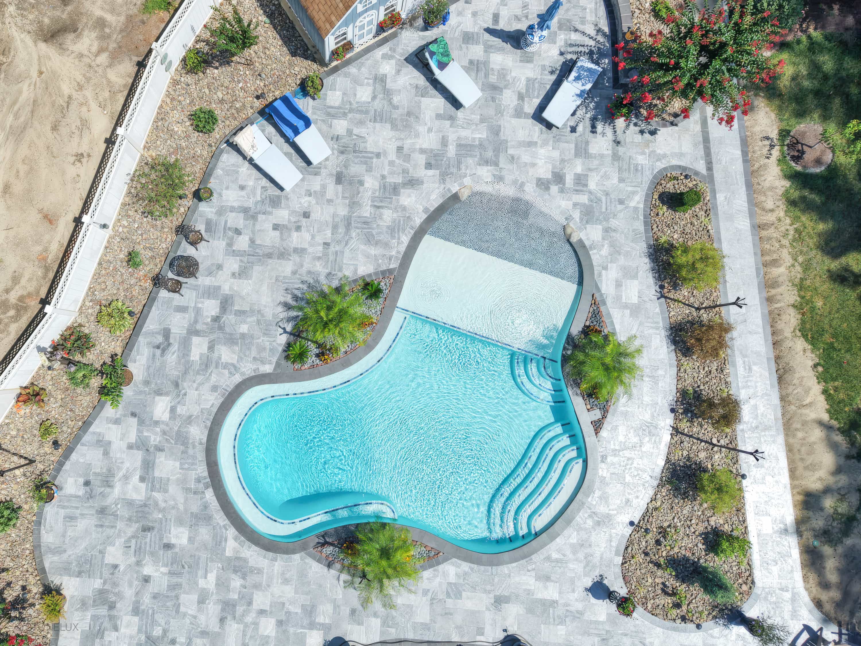 Aerial view of a modern pool retreat in Salisbury, MD, featuring Aegean Grey Marble pavers and Black Basalt coping. The vibrant blue pool with elegant stairs is surrounded by lush greenery, white lounge chairs, and a sleek patio, creating a luxurious o...
