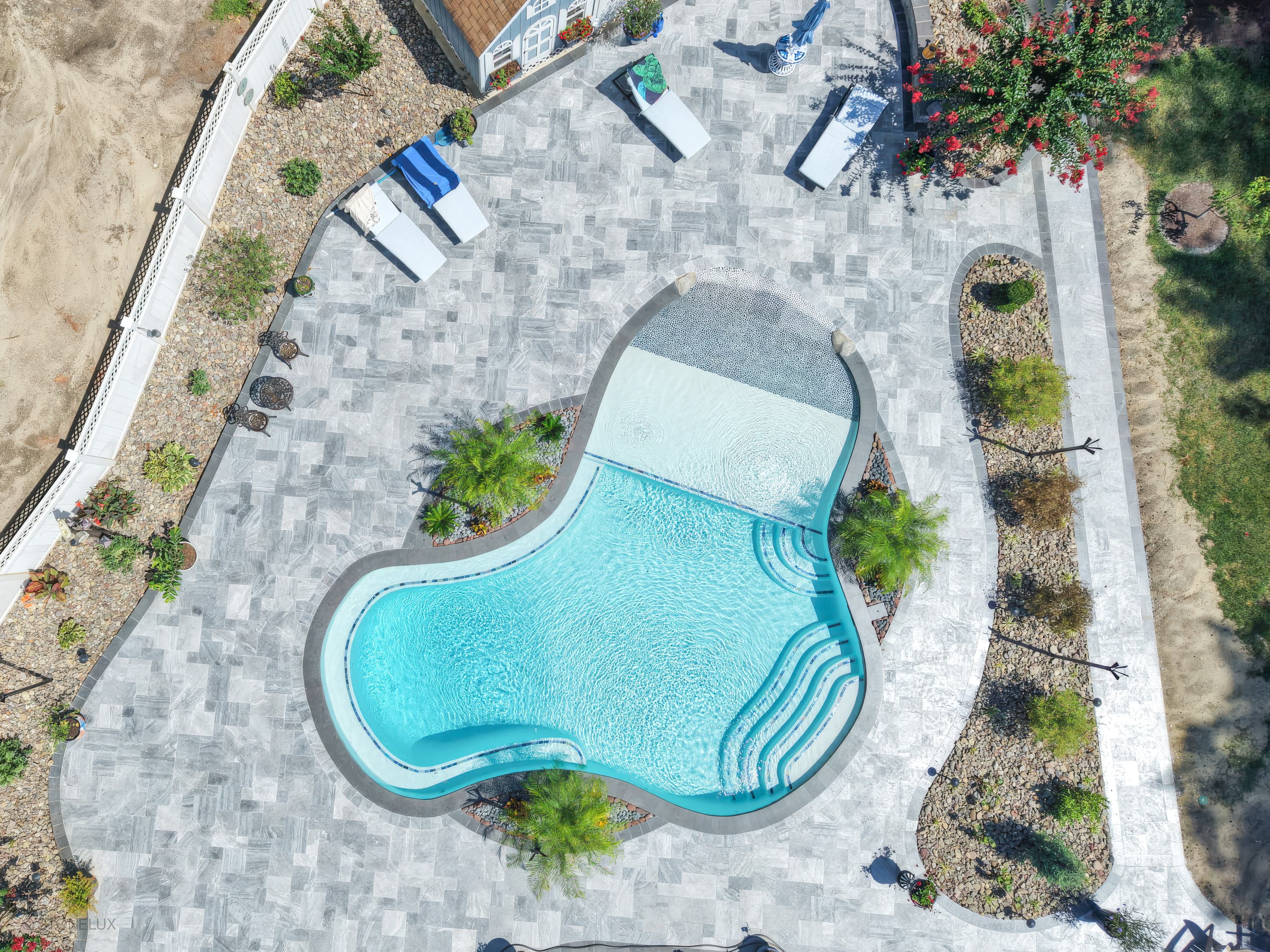 Aerial view of a modern pool retreat in Salisbury, MD, featuring Aegean Grey Marble pavers and Black Basalt coping. The vibrant blue pool with elegant stairs is surrounded by lush greenery, white lounge chairs, and a sleek patio, creating a luxurious o...
