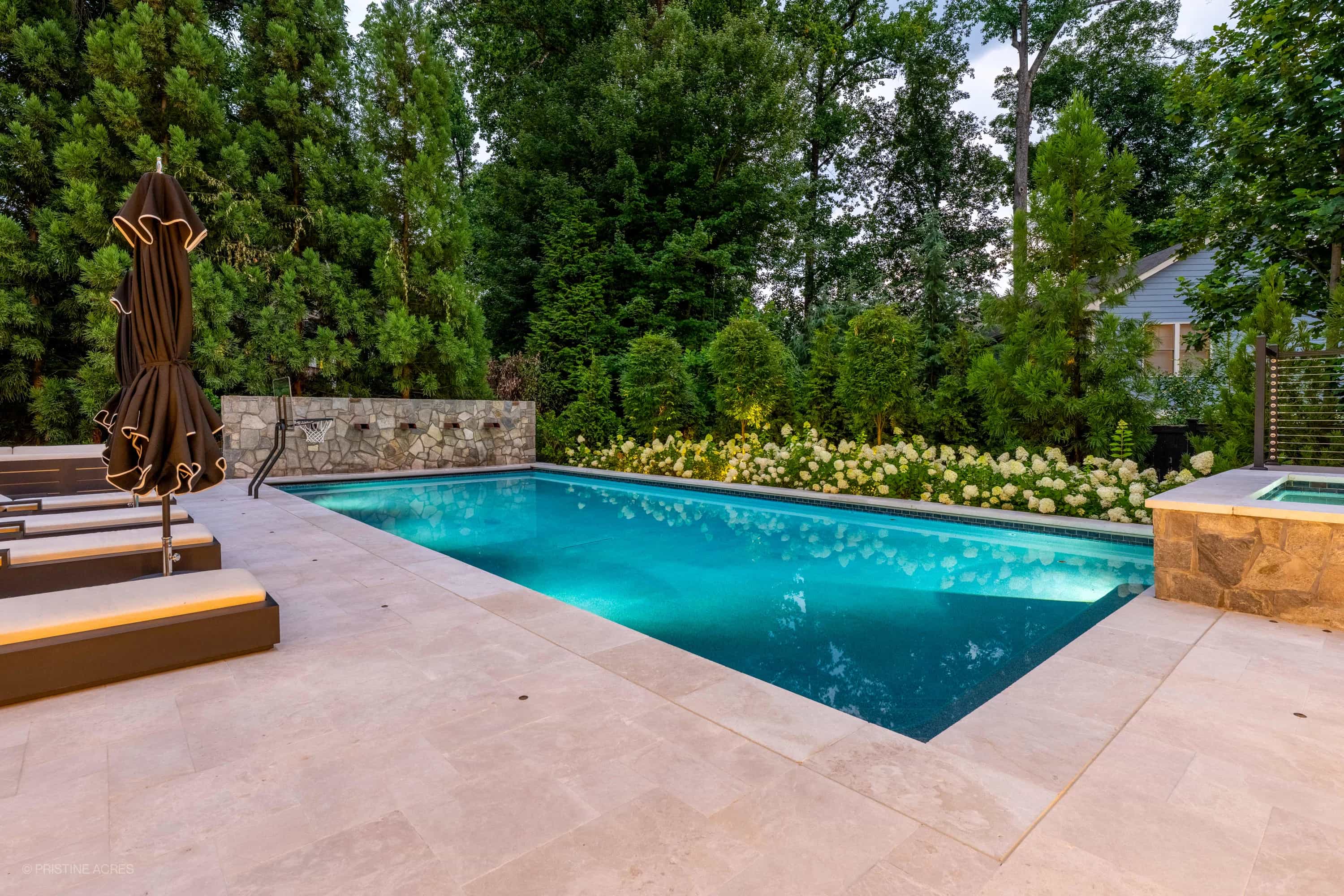Luxurious outdoor living space in McLean, VA featuring a Pera Cream Marble pool deck. The serene pool with vibrant blue water is surrounded by lush greenery and elegant lounge chairs, creating a modern, tranquil backyard oasis.