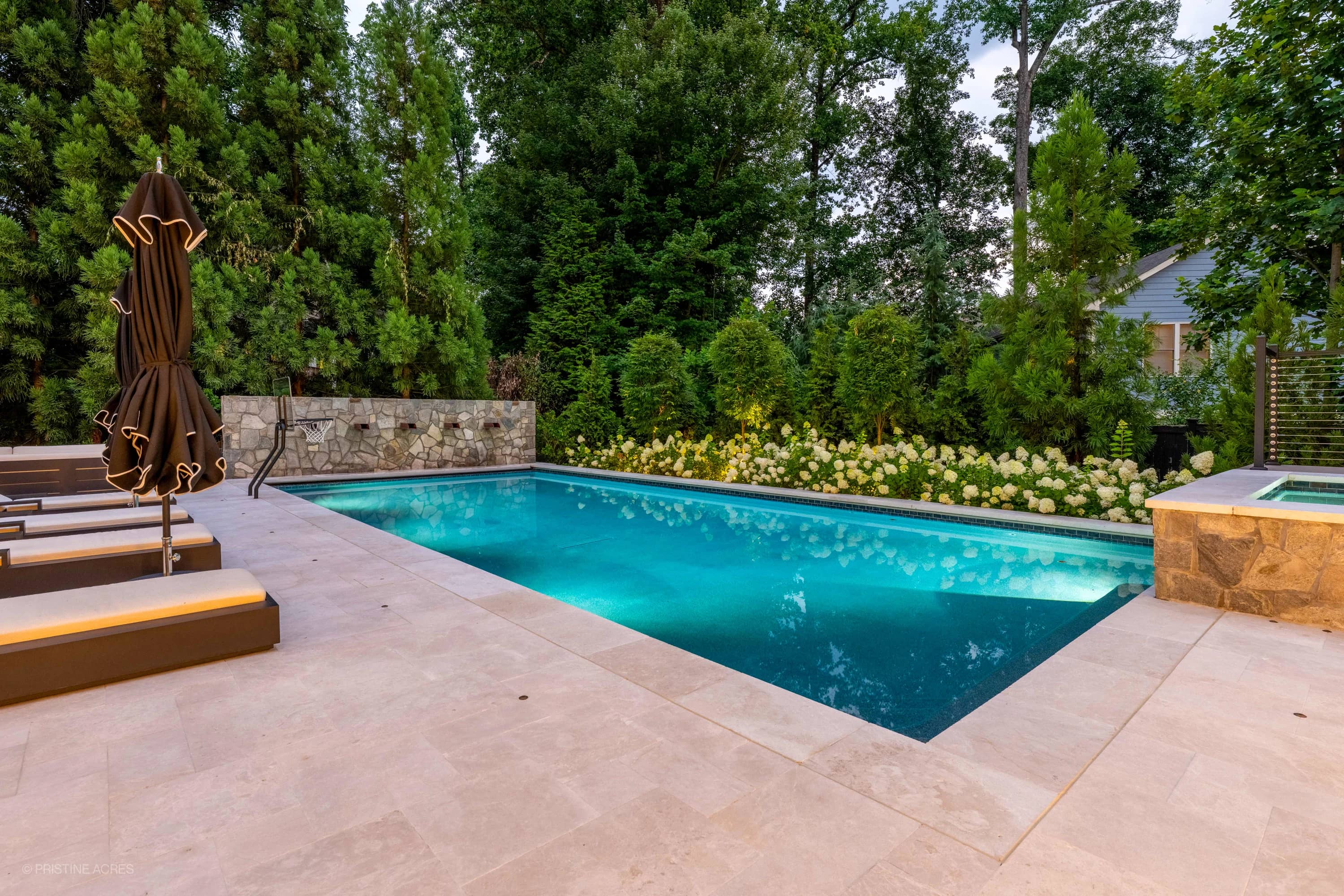 Luxurious outdoor living space in McLean, VA featuring a Pera Cream Marble pool deck. The serene pool with vibrant blue water is surrounded by lush greenery and elegant lounge chairs, creating a modern, tranquil backyard oasis.