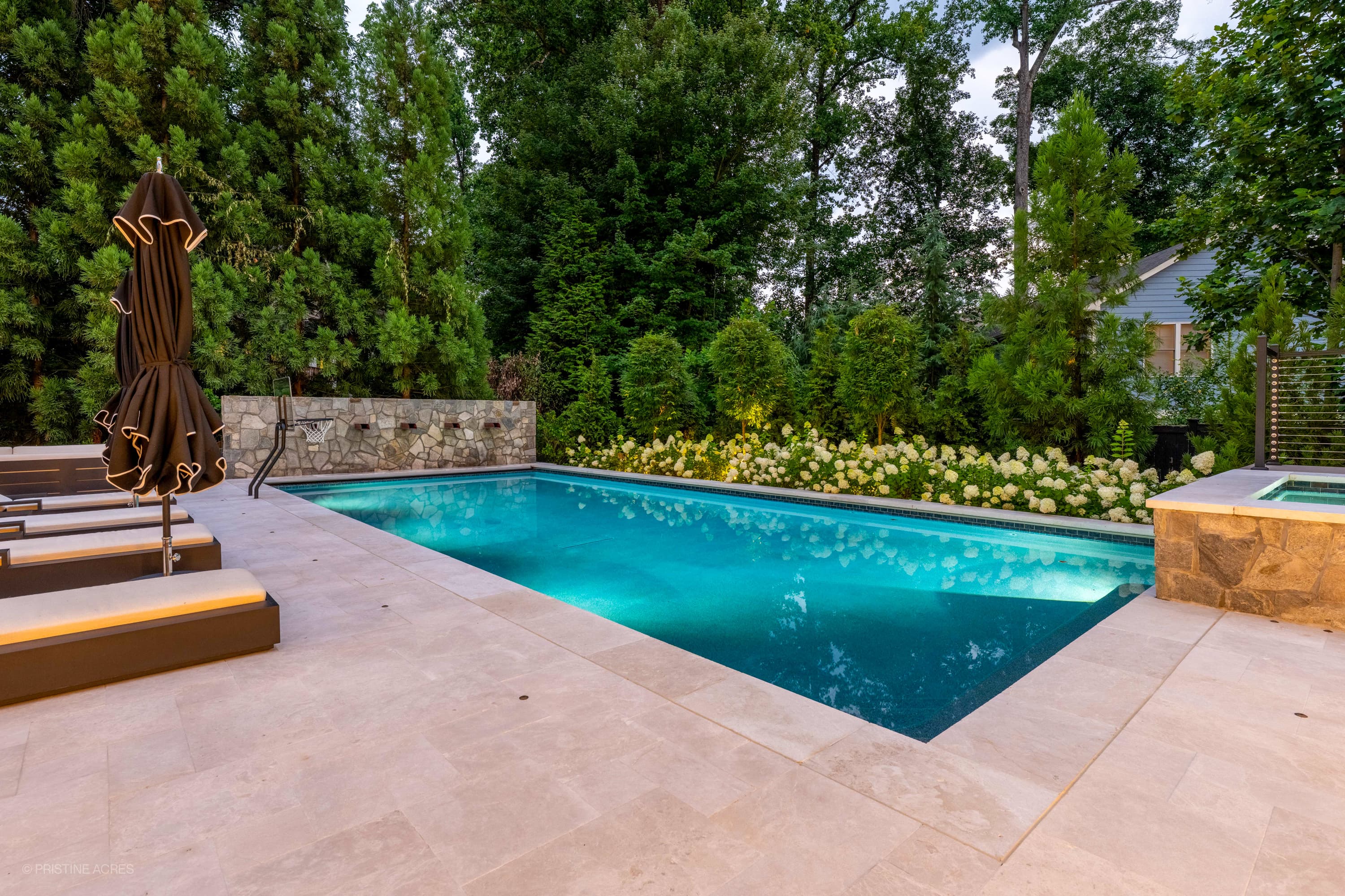 Luxurious outdoor living space in McLean, VA featuring a Pera Cream Marble pool deck. The serene pool with vibrant blue water is surrounded by lush greenery and elegant lounge chairs, creating a modern, tranquil backyard oasis.