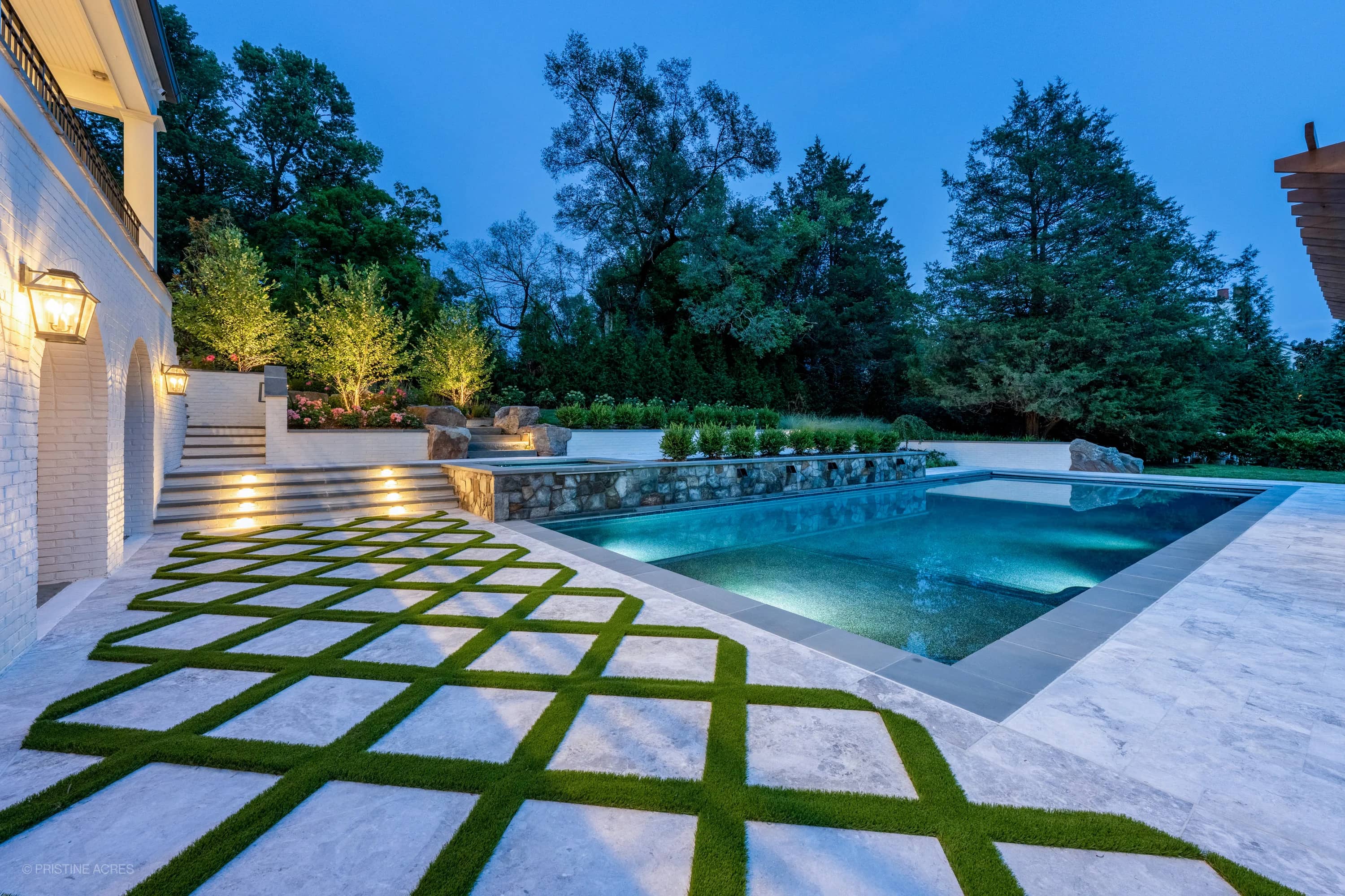 Luxurious Tundra Grey Marble pool deck with elegant Bluestone coping in McLean, VA. Modern design features a serene blue pool, lush greenery, and ambient lighting. Perfect for sophisticated outdoor spaces and hardscape projects.