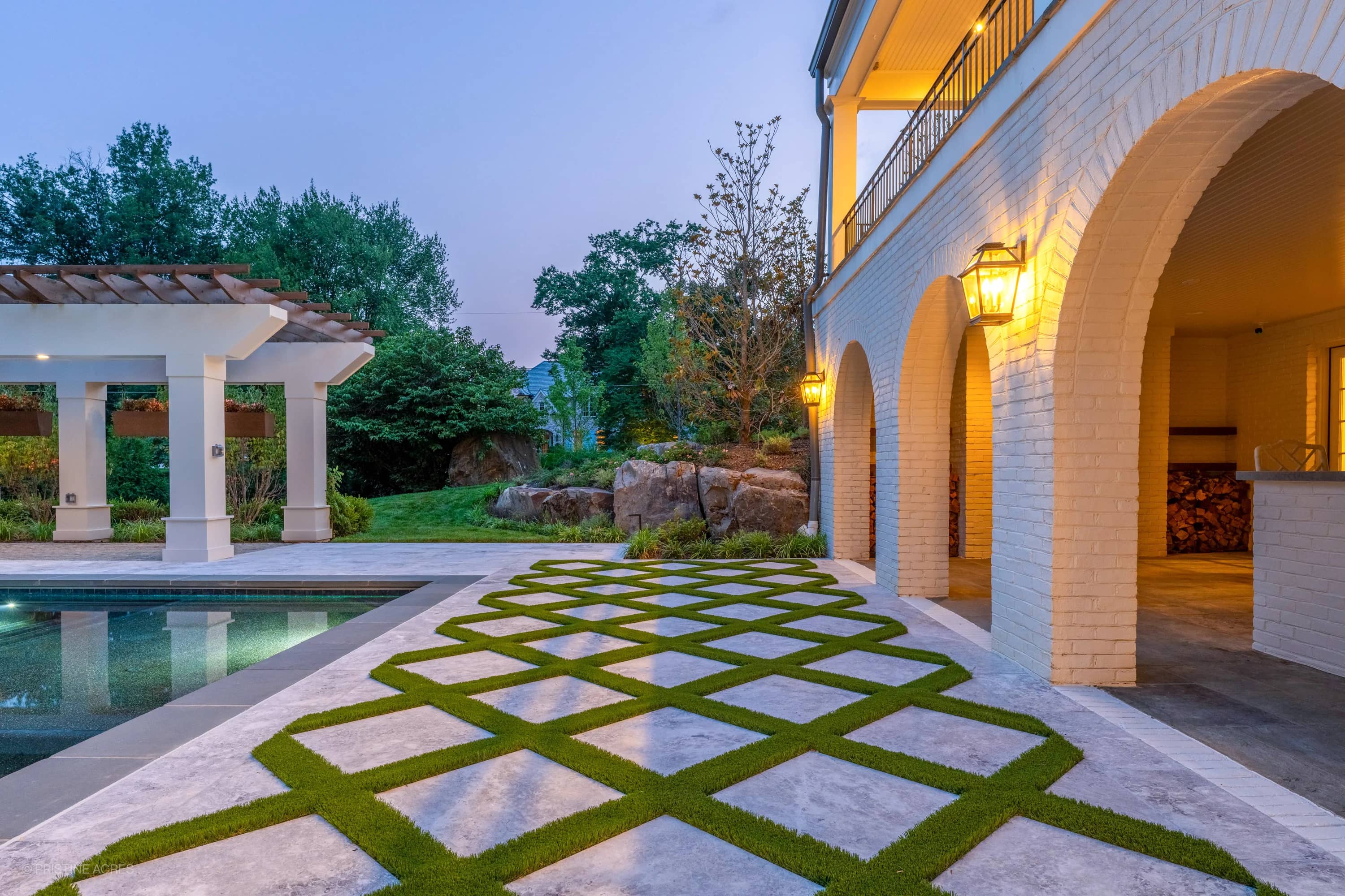Tundra Grey Marble pool deck with bluestone coping in McLean, VA. The contemporary design features a geometric pattern, lush greenery, and a serene pool with clear water. Elegant arches and ambient lighting enhance the tranquil backyard setting.