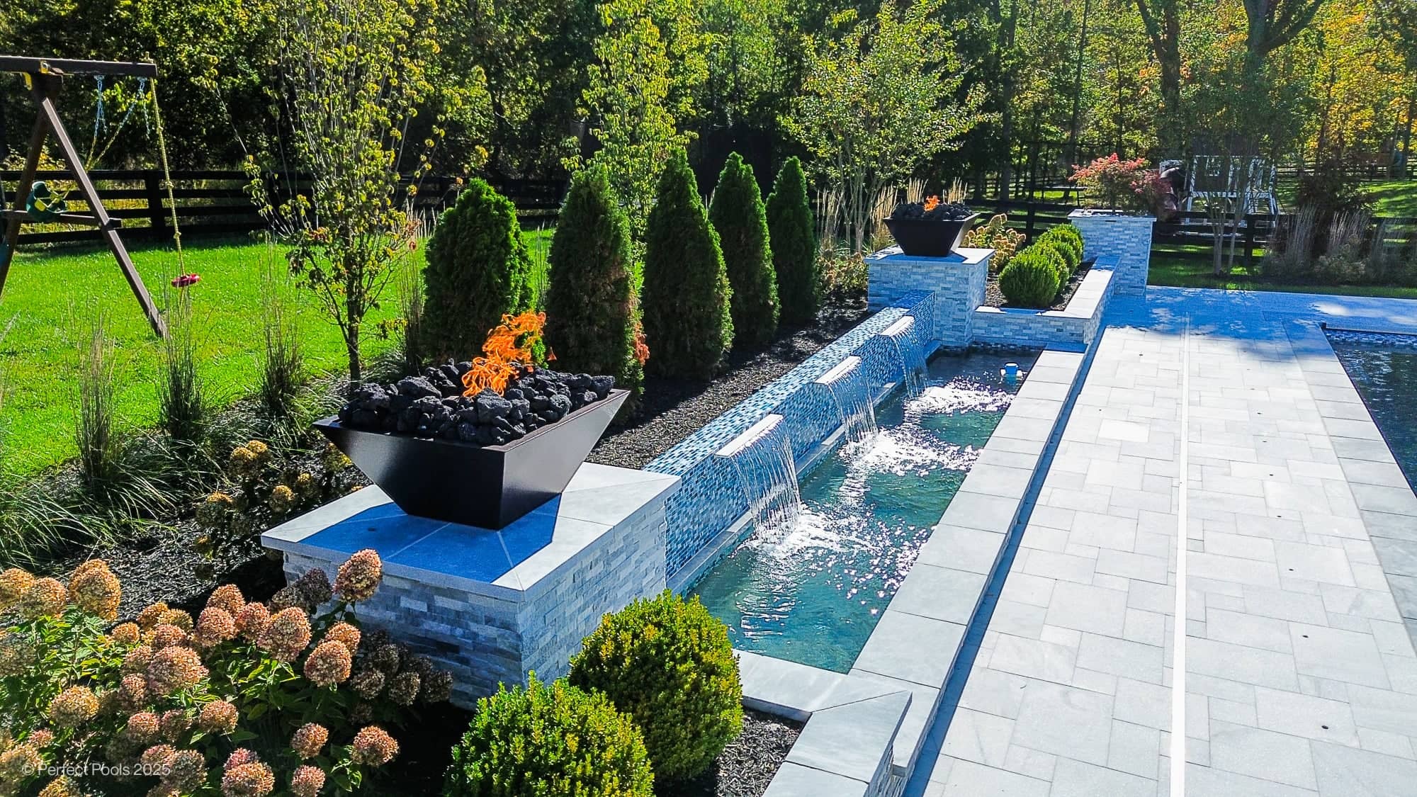 Luxury pool project in Aldie, VA featuring Aldie Serenity with Afyon White and Arctic Grey Marble. Modern design with sleek water features, lush greenery, and elegant landscaping. Grey marble pavers harmonize with tranquil blue pool water.