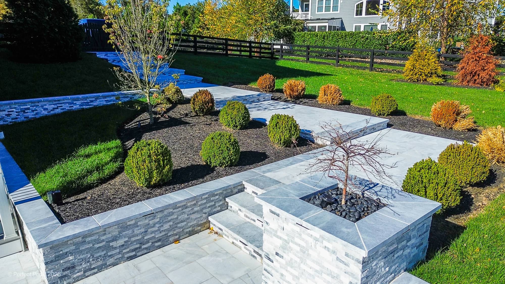 Aldie Serenity showcases Afyon White and Arctic Grey marble in a luxurious poolside setting. Modern design with sleek marble pavers, manicured shrubs, and vibrant greenery. The elegant landscape features layered stone planters, enhancing the serene bac...