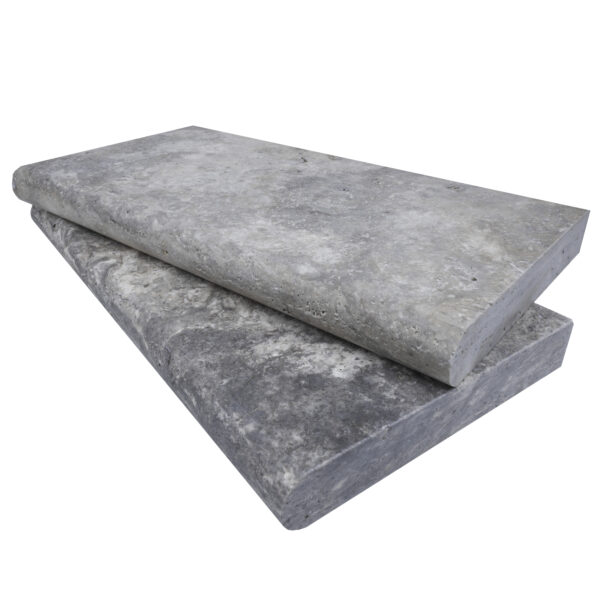 Two large Silver Travertine Tumbled 12"x24"x2" Single Bullnose Copings stacked on top of each other, isolated on a white background, showing textured surfaces.