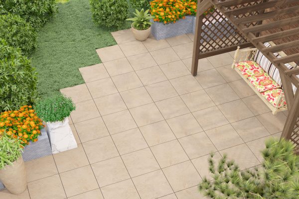 A landscaped garden featuring a Bavaria Beige 24"x24" 2CM Matte Rectified Porcelain Paver patio area with a wooden pergola, a bench with colorful cushions, green shrubs, and potted plants. Clear sunny day.
