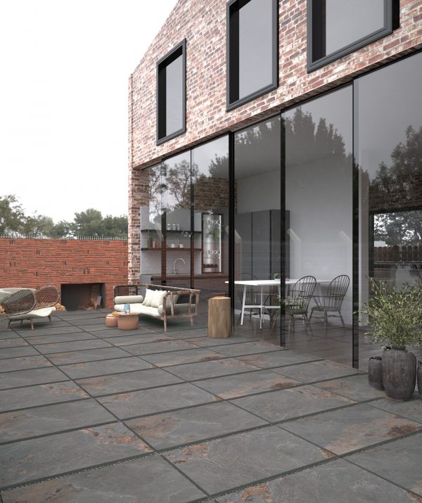 A modern brick house with large glass windows and doors leading to a patio with Vintage Stone 24"x36" 2CM Matte Rectified Porcelain Pavers. A dining area is visible through the glass, and pottery decorates the scene.