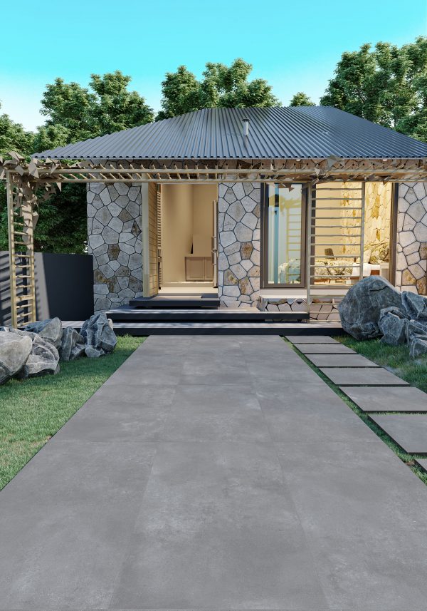 Modern backyard patio features a textured Luna Cool Gray 24"x24" 2CM Matte Rectified Porcelain Paver walkway leading to a house with large glass doors and stone walls under a corrugated metal roof, framed by a wooden pergola.