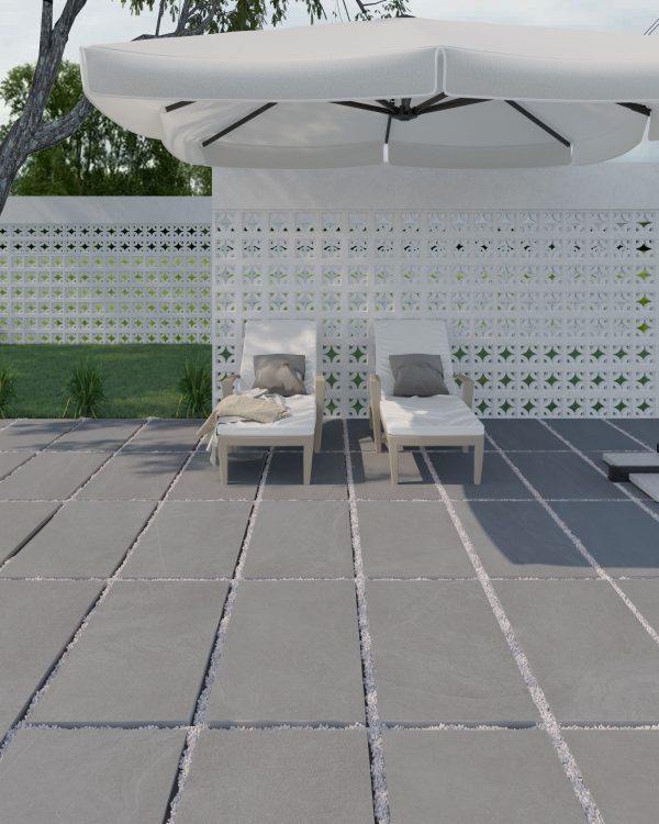 Onda Pearl 24"x48" 2CM Matte Rectified Porcelain Pavers under a large umbrella on a porcelain paver patio, surrounded by a white lattice fence and green bushes, with trees and sky in the background.