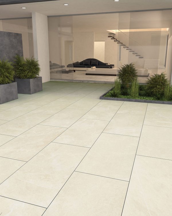 A spacious, modern lobby with large Onda Sand 24"x48" 2CM Matte rectified porcelain pavers and glass walls, featuring green plants in rectangular pots and a minimalist staircase leading to an upper level with a view of a sleek black sofa