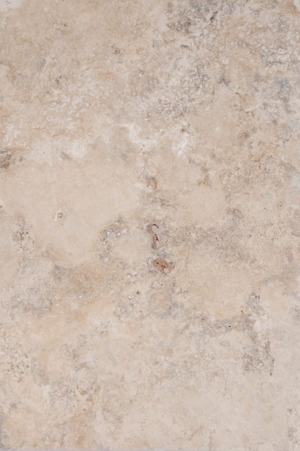 Close-up view of a textured Premium Philly Travertine Tumbled 16x24 3cm Paver surface with a soft blend of beige and light gray tones, featuring intricate natural patterns and small pits.