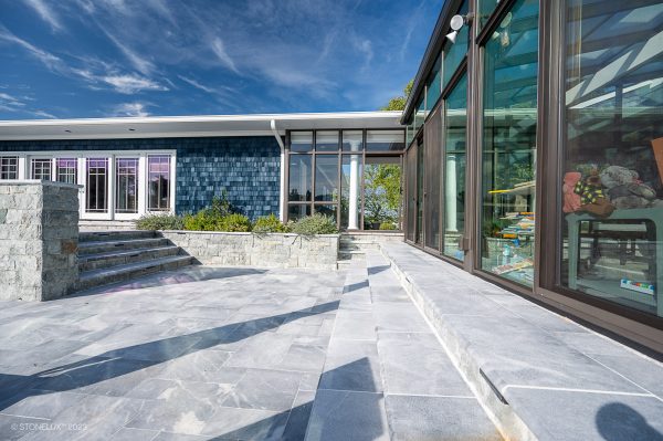 Modern house exterior with large, clear glass windows, an Arctic Grey Marble Sand Blasted Bullnose Copings as steps, and a distinctive blue tile feature on the facade under a clear blue sky.