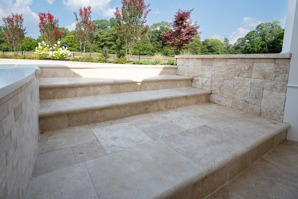 Ivory Travertine Tumbled 12"x24"x2" Single Bullnose Coping - Premium steps leading to a landscaped garden with lush greenery and flowering trees, viewed on a sunny day.